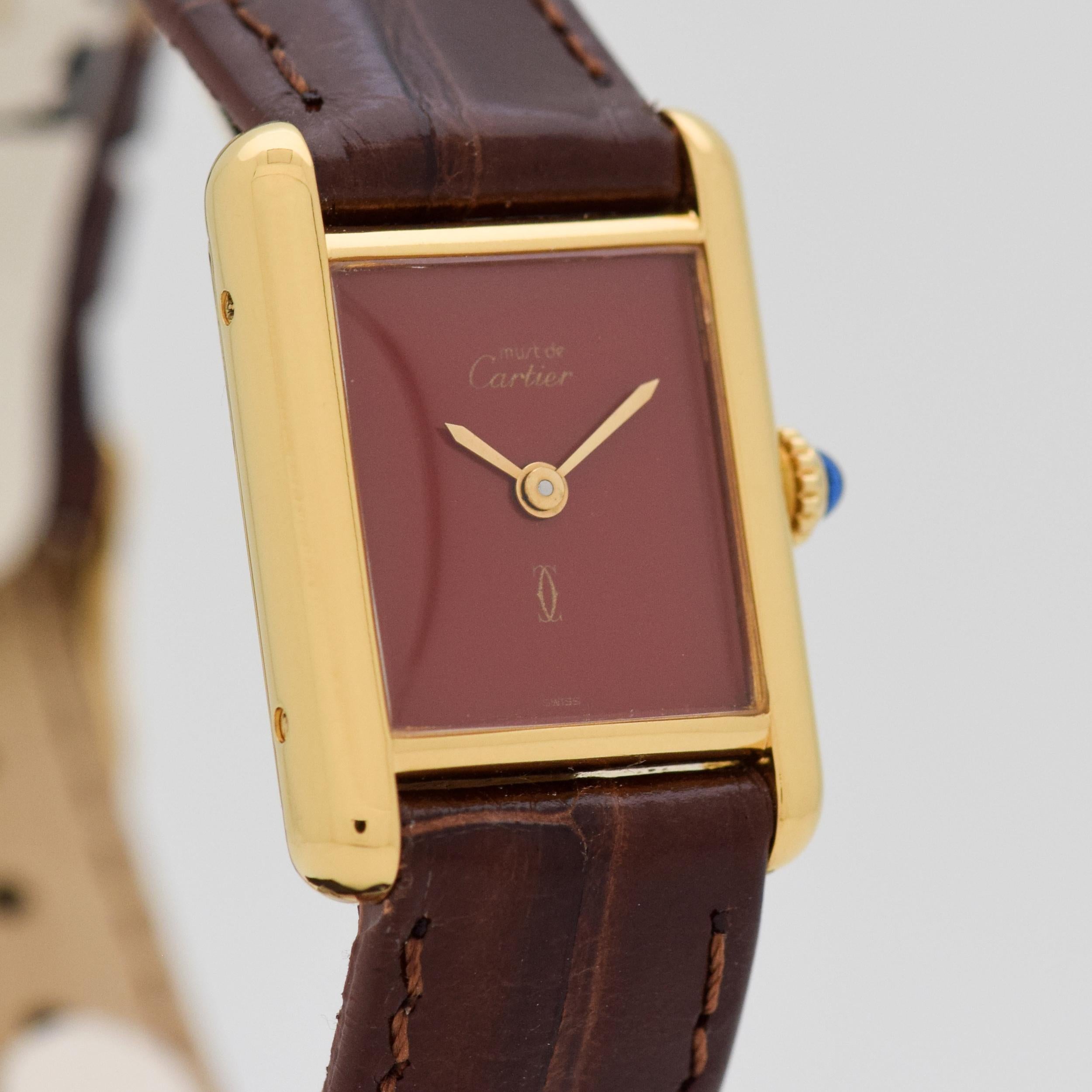 1990's Cartier Standard Ladies Size Must de Tank 18k Yellow Gold Electroplated Over Sterling Silver case Mechanical Wind watch with Original Red/Maroon Dial. Case size, 20mm x 27mm lug to lug (0.79 in. x 1.06 in.) - Powered by a 17-jewel, manual