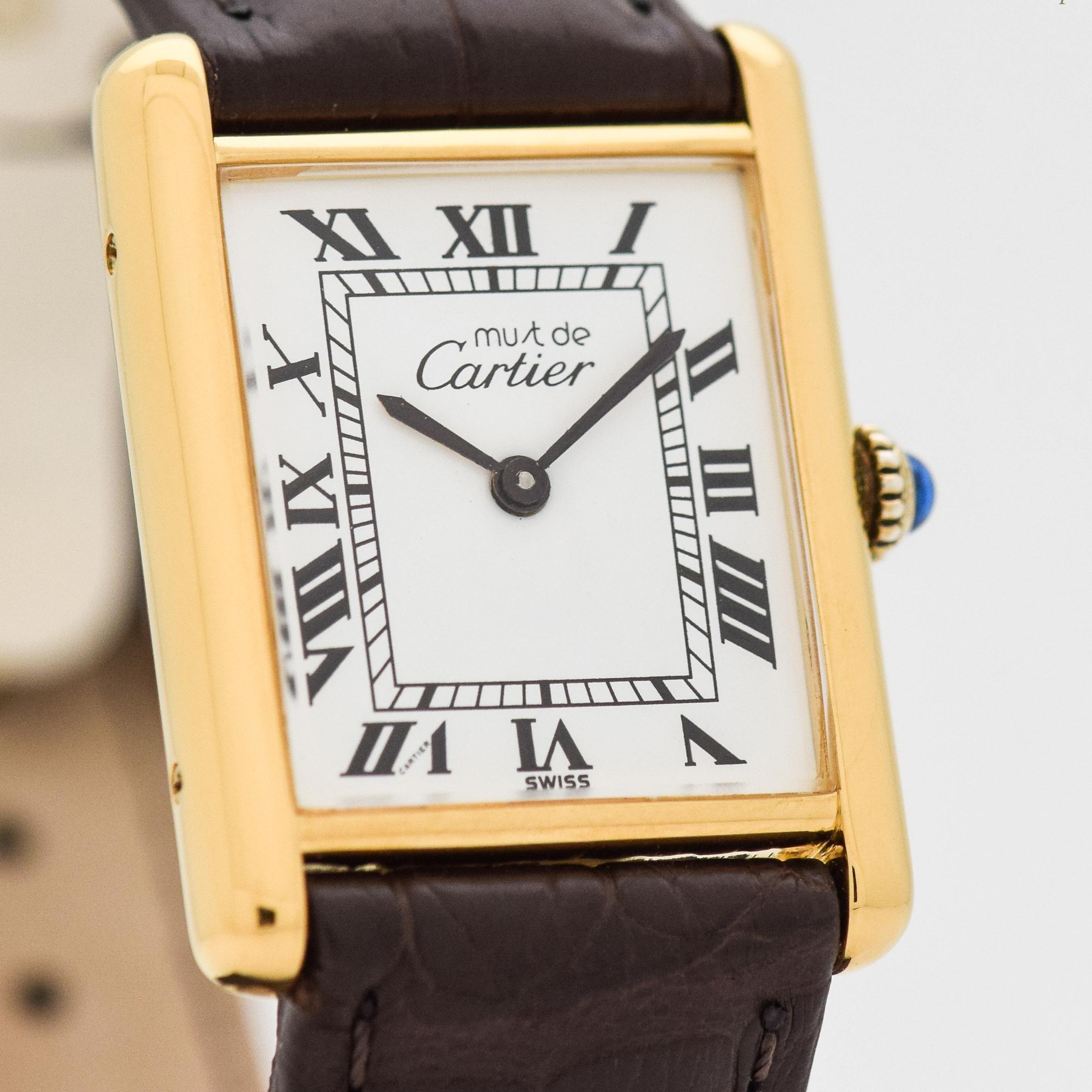 1990's era Cartier Tank Must de Men's Sized Watch. 18K Yellow Gold plated over Sterling Silver case. White dial with black-colored, Roman numerals. Powered by a 17-jewel, manual caliber ETA movement. 23mm x 30mm lug to lug (0.91 in. x 1.18 in.) -