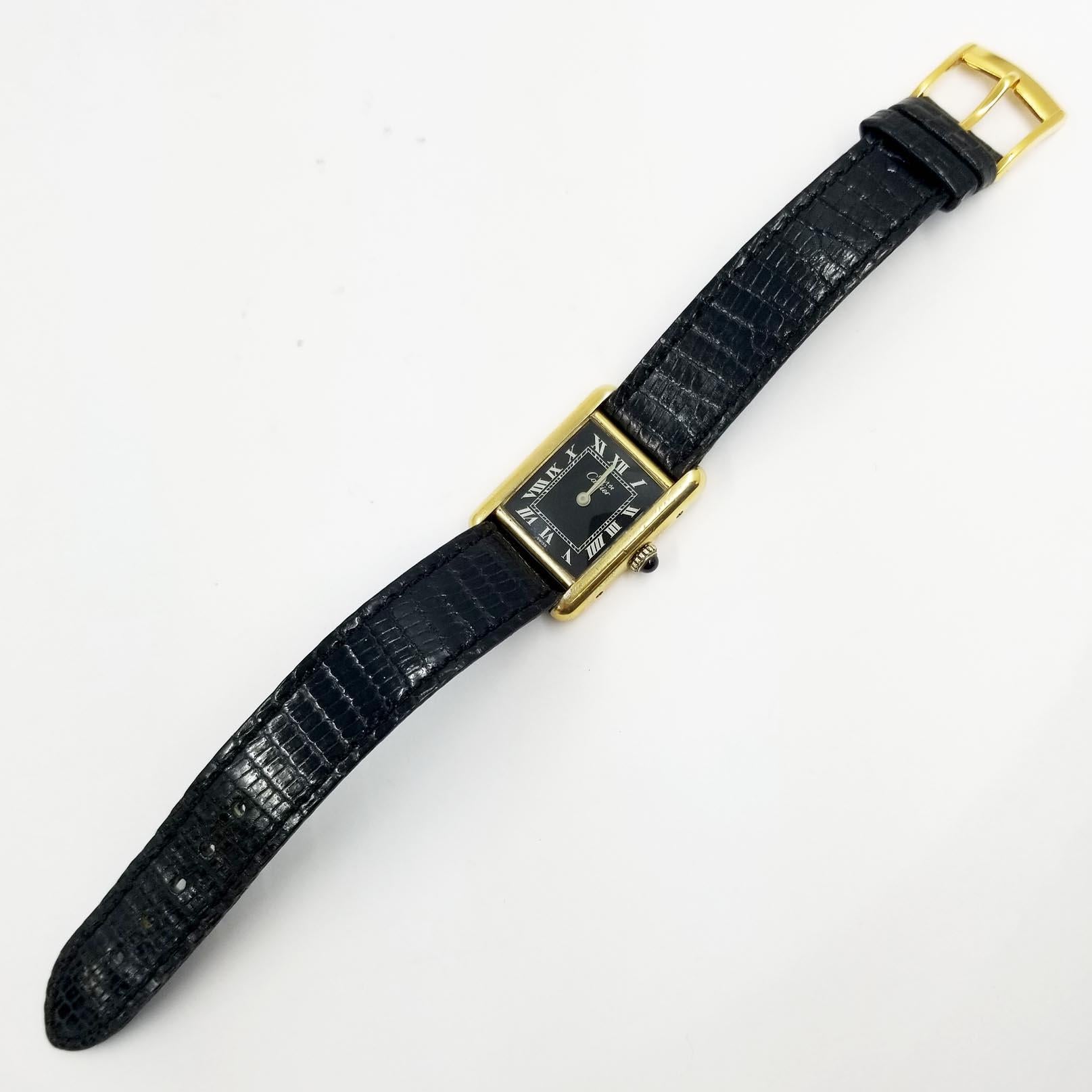 This rare vintage Cartier Tank wristwatch contains a manual wind movement. The dial is a black background with white roman numeral indicators. The strap is original, in black leather. The movement was recently serviced by a watchmaker, and comes