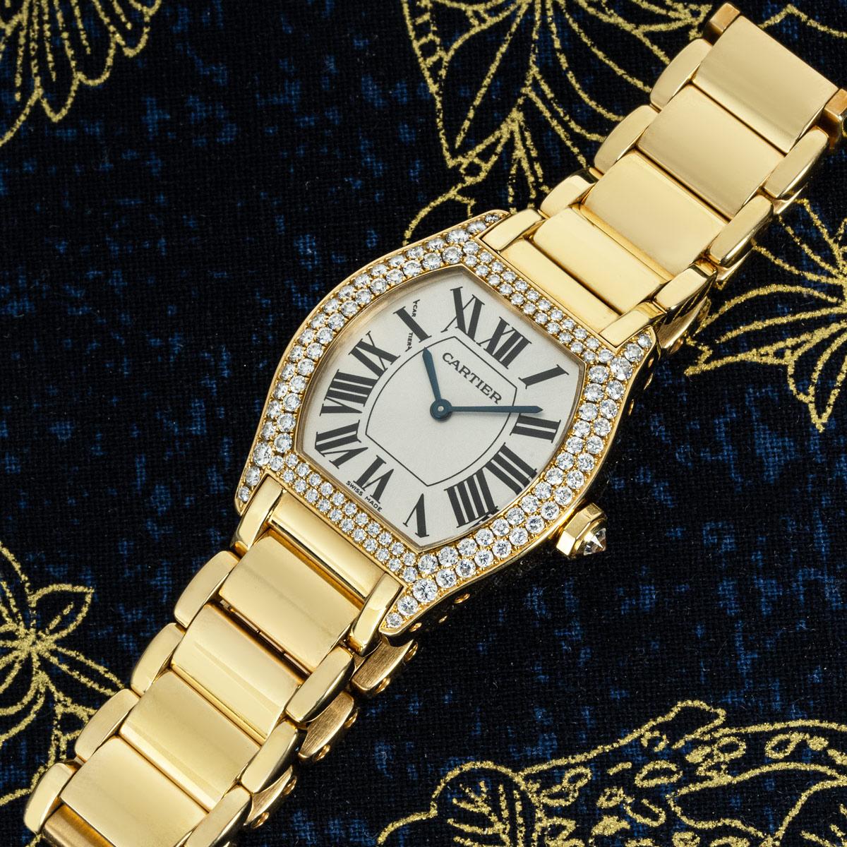 A Tortue wristwatch in yellow gold by Cartier. Features a silver dial with Roman numerals, sword-shaped hands in blued steel, and a Cartier signature hidden at 10 o'clock. Complementing the dial is the yellow gold bezel set with 118 round brilliant