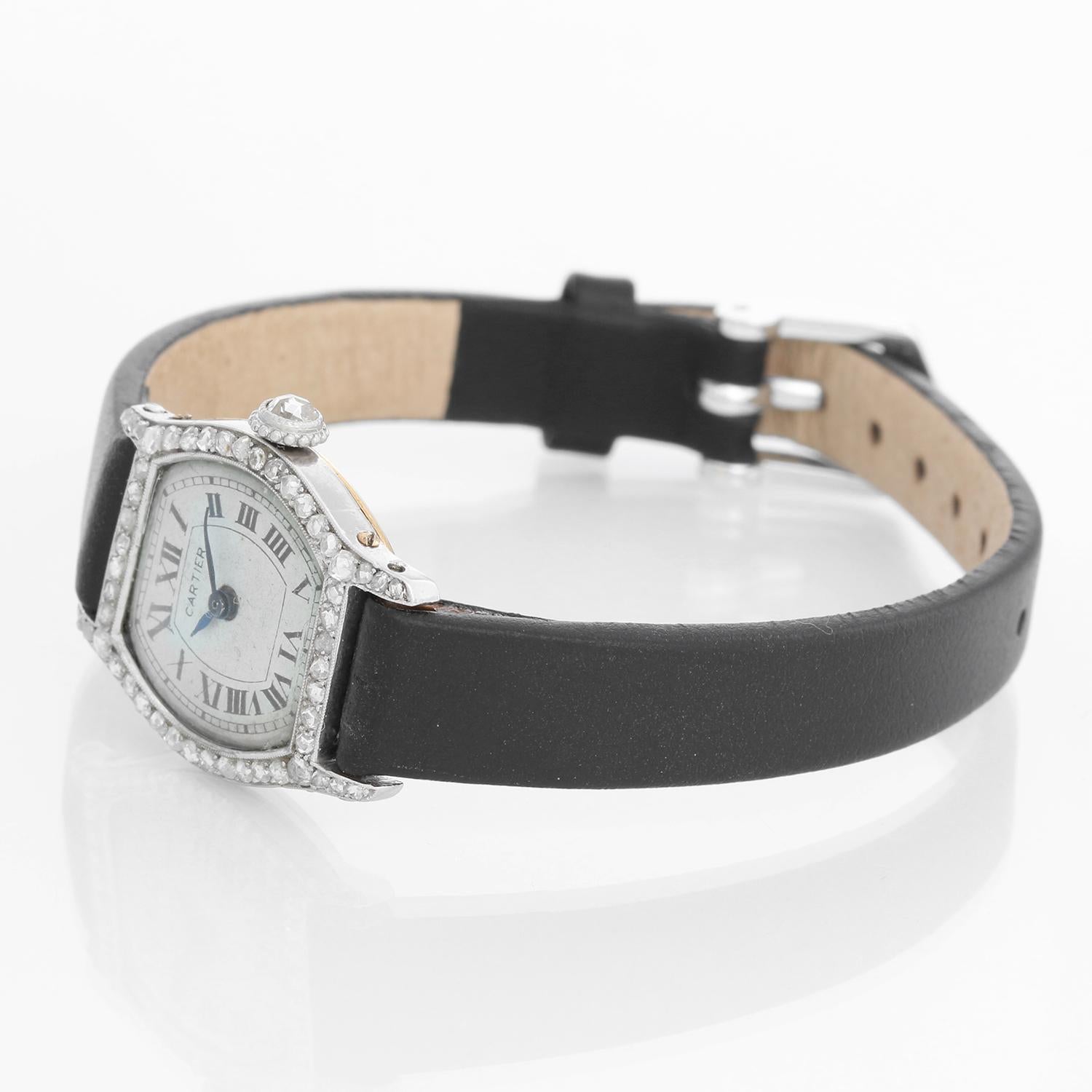 Cartier Tortue Ladies Platinum Watch - Manual winding. Platinum case with diamonds with a yellow gold caseback( 20 mm x 27mm). White dial with roman numerals. Black leather strap with tang buckle. Pre-owned with custom box. Circa 1920's. 