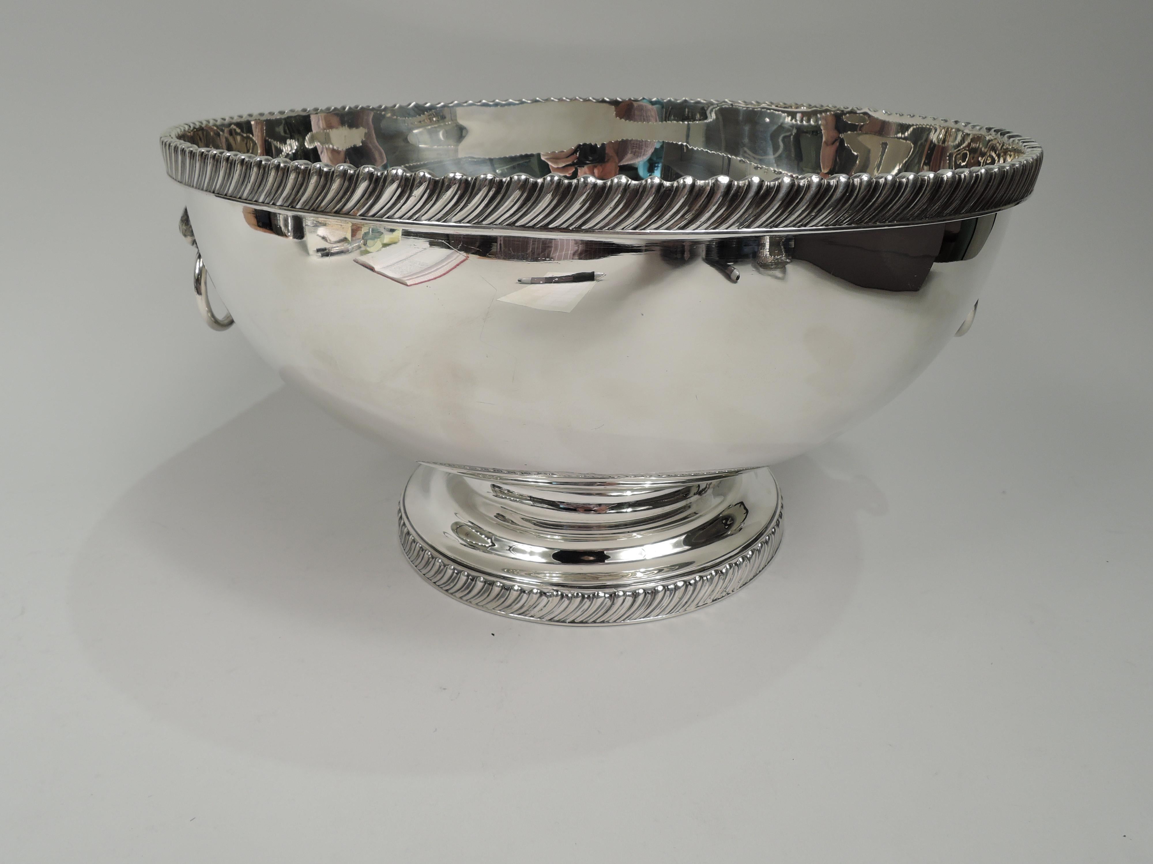 Traditional Georgian sterling silver bowl. Retailed by Cartier in New York. Curved sides and raised foot. Cast lion’s head mounts with loose rings. Cast gadrooned rims. Old fashioned and substantial with plenty of room for engraving. Perfect for