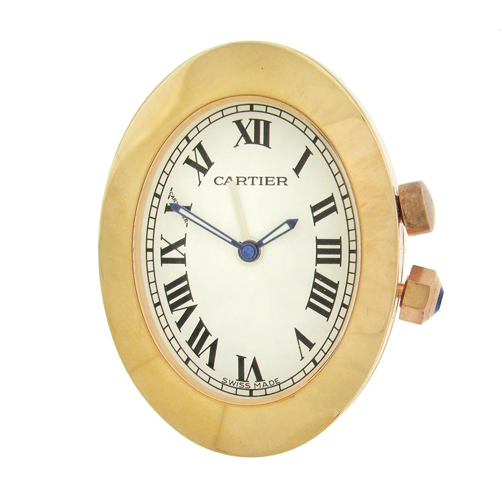 Sleek oval Cartier quartz travel clock has a wide bezel, white dial with black painted Roman numerals and secret Cartier signature at X, sapphire set crown to set alarm and time, and upper on/off alarm button. Gold plated  with stainless steel back,