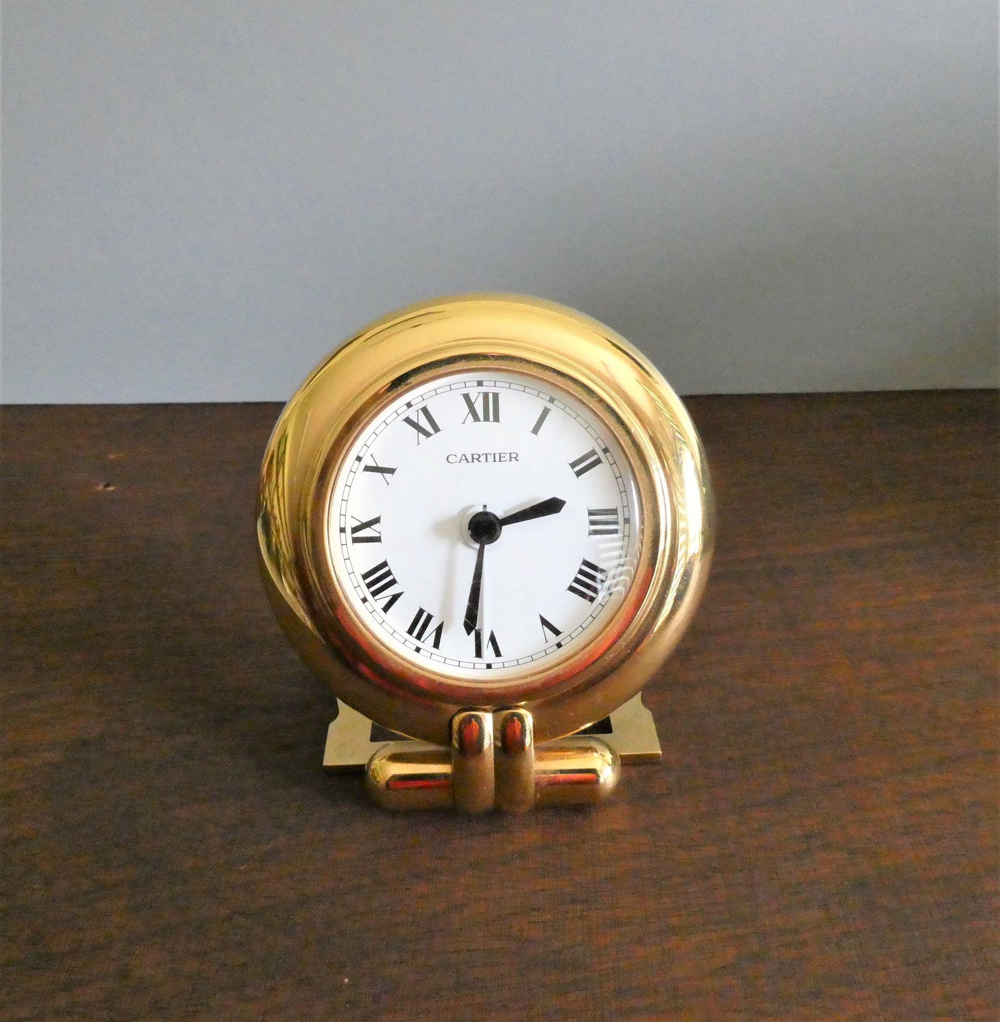 Travel Alarm Clock by Cartier
 
The clock housed in a round brass frame with decorative hinged strut support.
Painted dial with Roman numerals, original hands and alarm hand signed ‘Cartier’.
The circular steel back of the clock signed ‘Cartier’