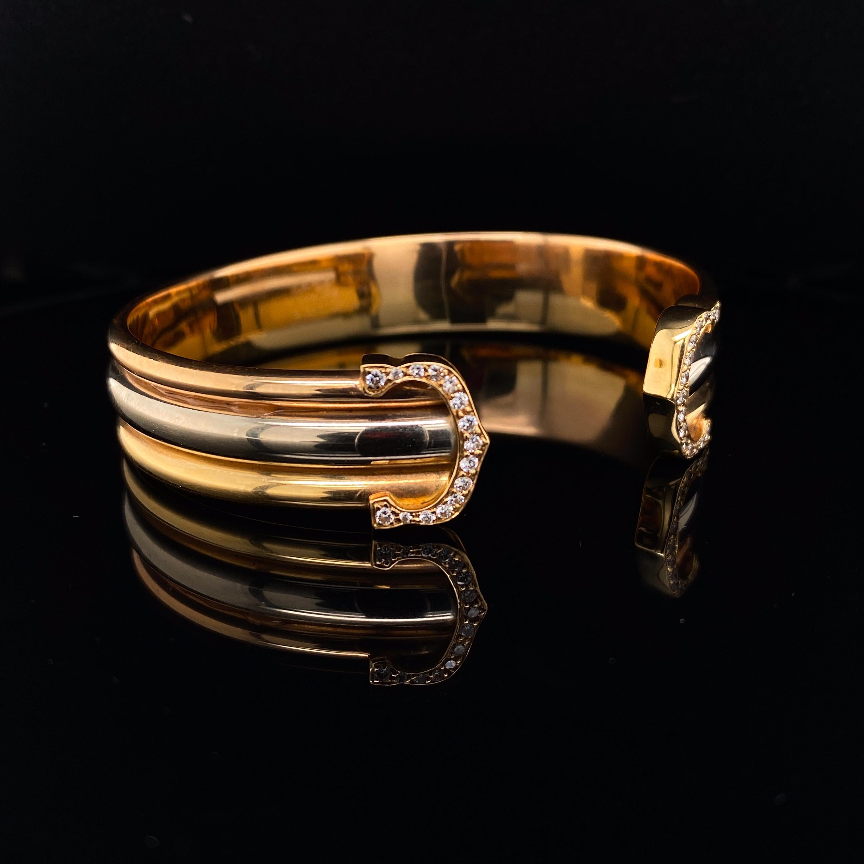 Cartier Trinity 18 Karat Yellow White and Rose Gold Cuff Bracelet

This classic, wearable Cartier Trinity tri-colour gold open cuff bracelet features two diamond set C's, one terminating either end of the piece.
The round brilliant cut diamonds are