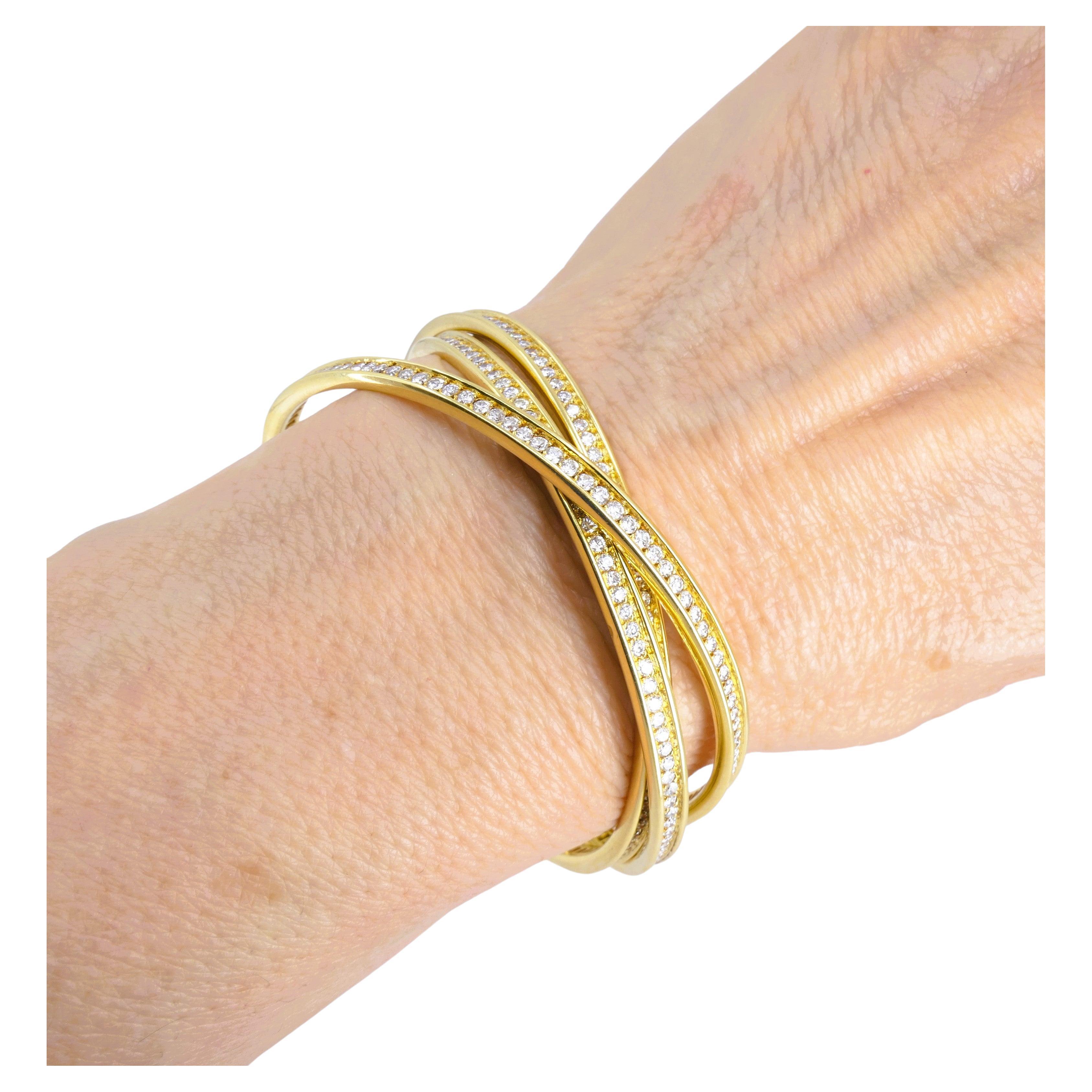 Bracciale Cartier Trinity in oro 18 carati e diamanti rotondi a taglio pieno.
Il pezzo è composto da tre braccialetti bangle intrecciati. I diamanti sono incastonati a quattro punte e corrono lungo tutta la lunghezza dei bracciali. I bracciali