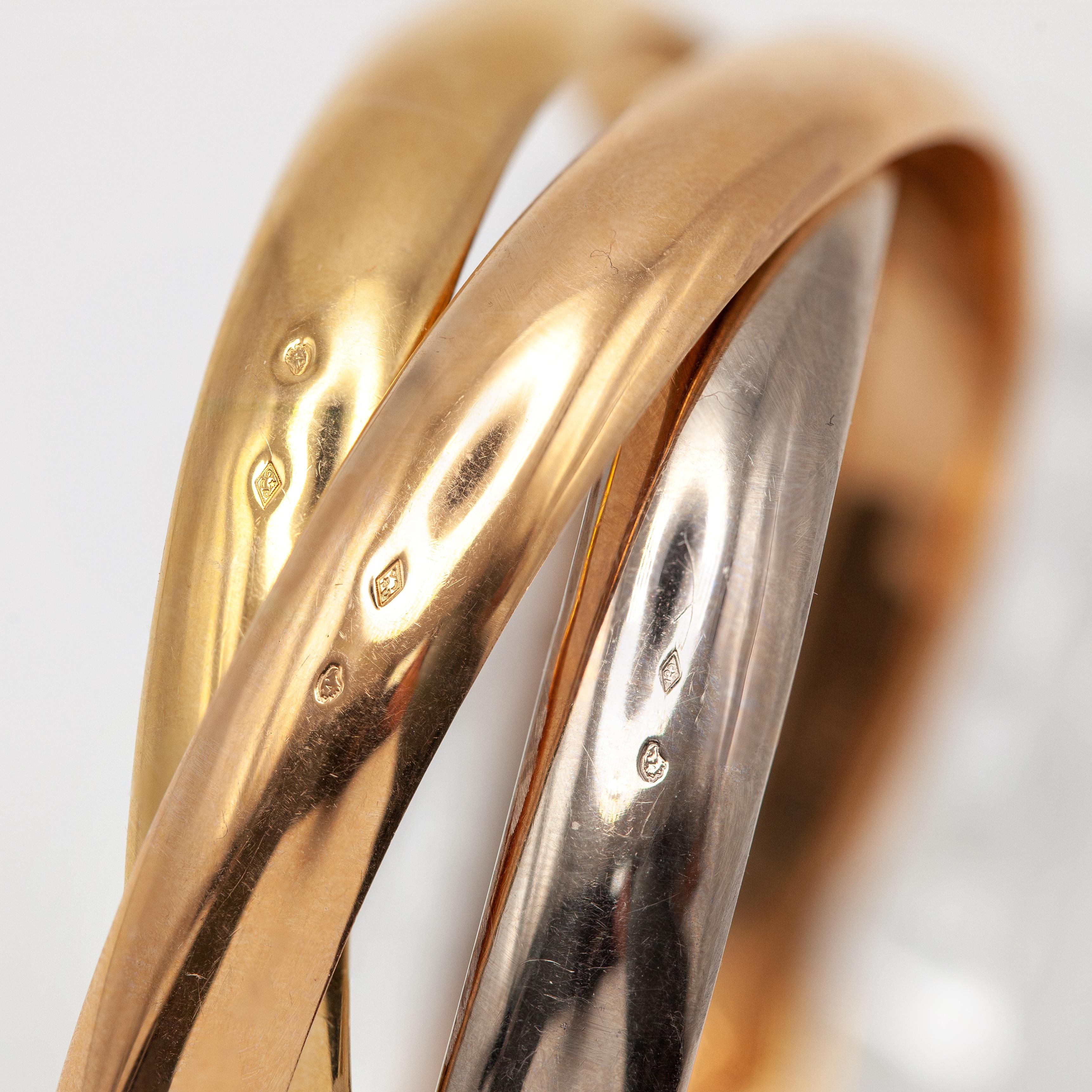 An iconic Cartier Trinity bangle bracelet, expertly crafted in solid 18 karat yellow gold, white gold, and rose gold, featuring the house’s celebrated interlocking three-band design. The fluid, sculptural form allows each polished gold band to move