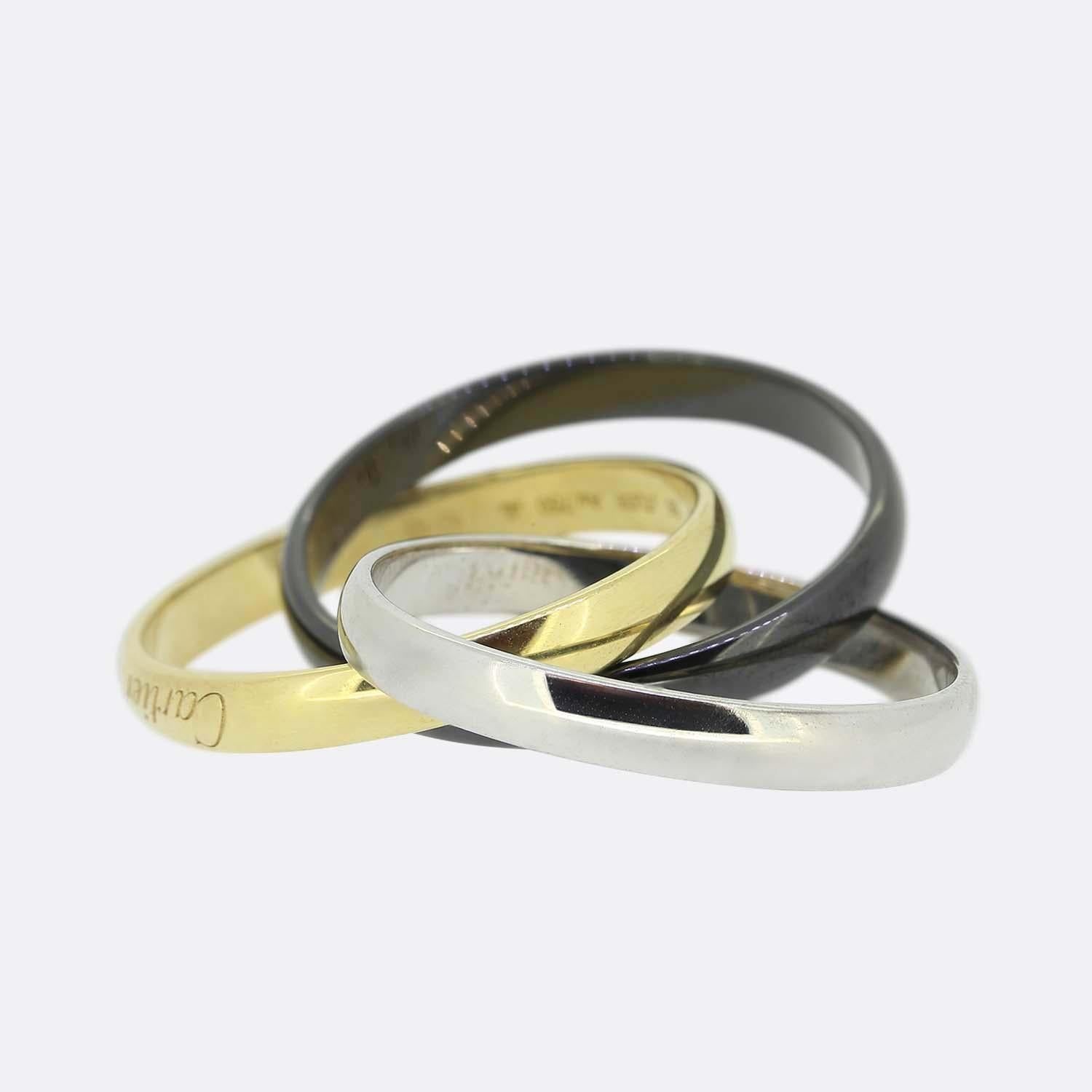 Here we have an 18ct gold and ceramic trinity ring from the world renowned luxury jewellery house of Cartier. This ring features three interwinding bands. One white gold, one yellow gold and one in darkened ceramic. The yellow gold has been softly