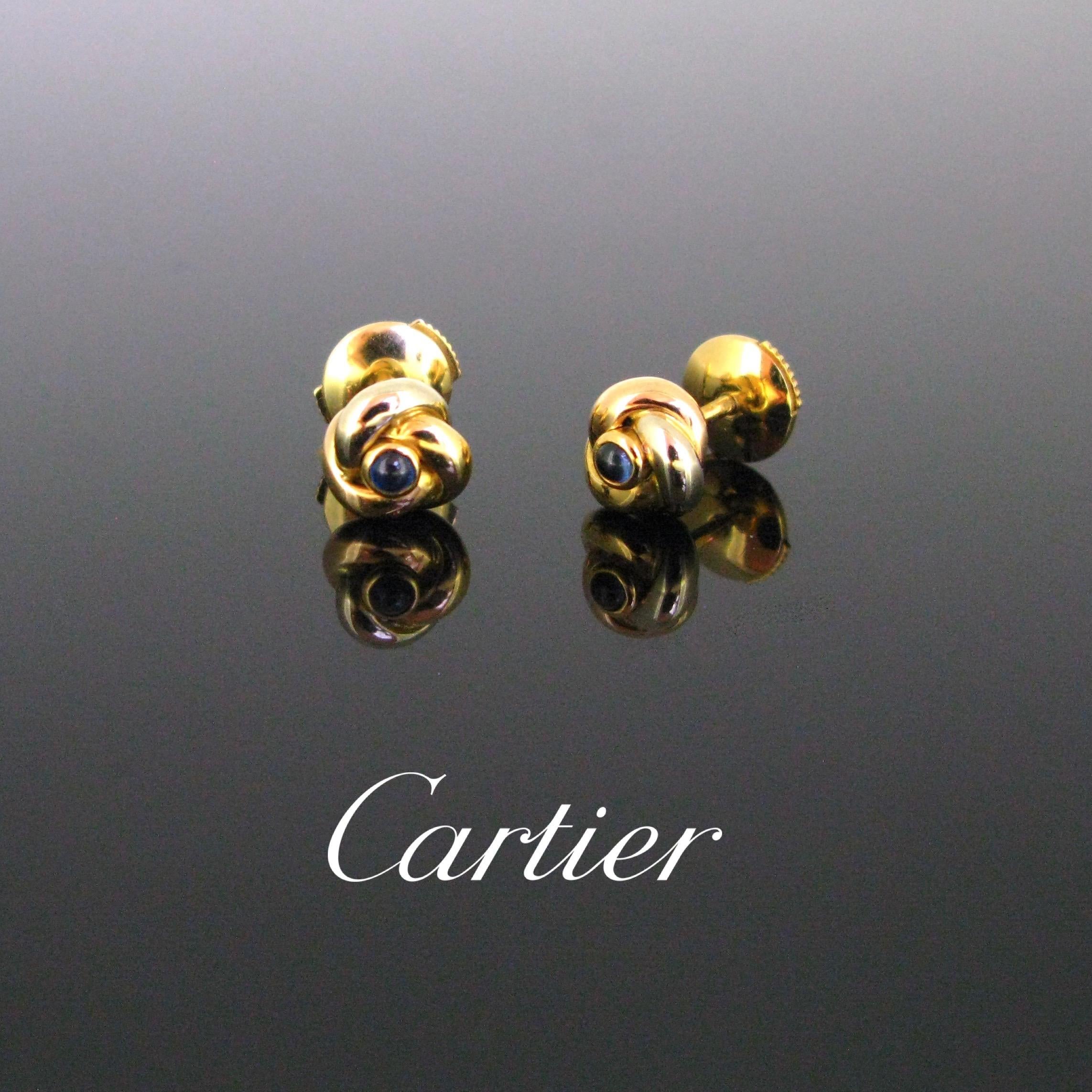 This pretty pair of earrings by Cartier is from the famous Trinity collection. The earrings are made in 18kt gold - white, yellow and rose. They are set with a blue sapphire cabochon in the centre. The earrings come in their original Cartier