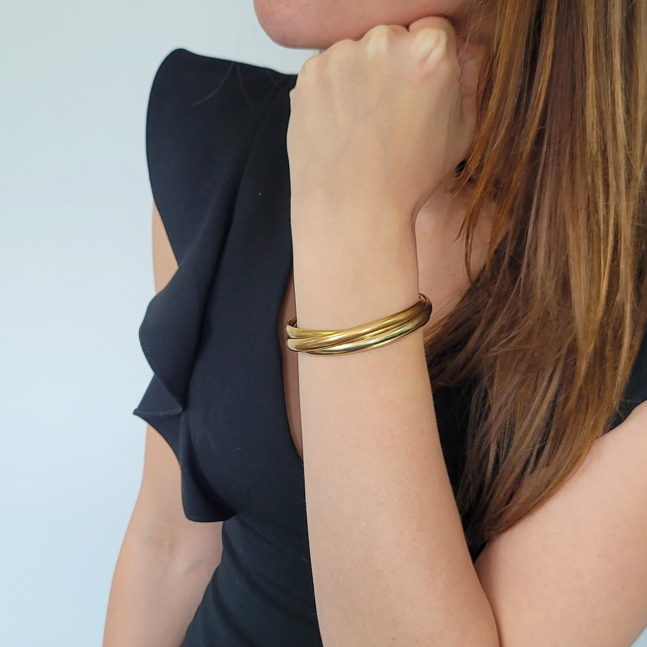 Braccialetto bangle Cartier Trinity in oro 18 carati tri-tono. Consiste in
tre fasce: Oro giallo 18 carati, oro rosa 18 carati e bianco 18 carati.
d'oro, incastrati l'uno nell'altro. Con dedica:
Cartier, 750, 203705, 
Taglia 62. 
Larghezza di una