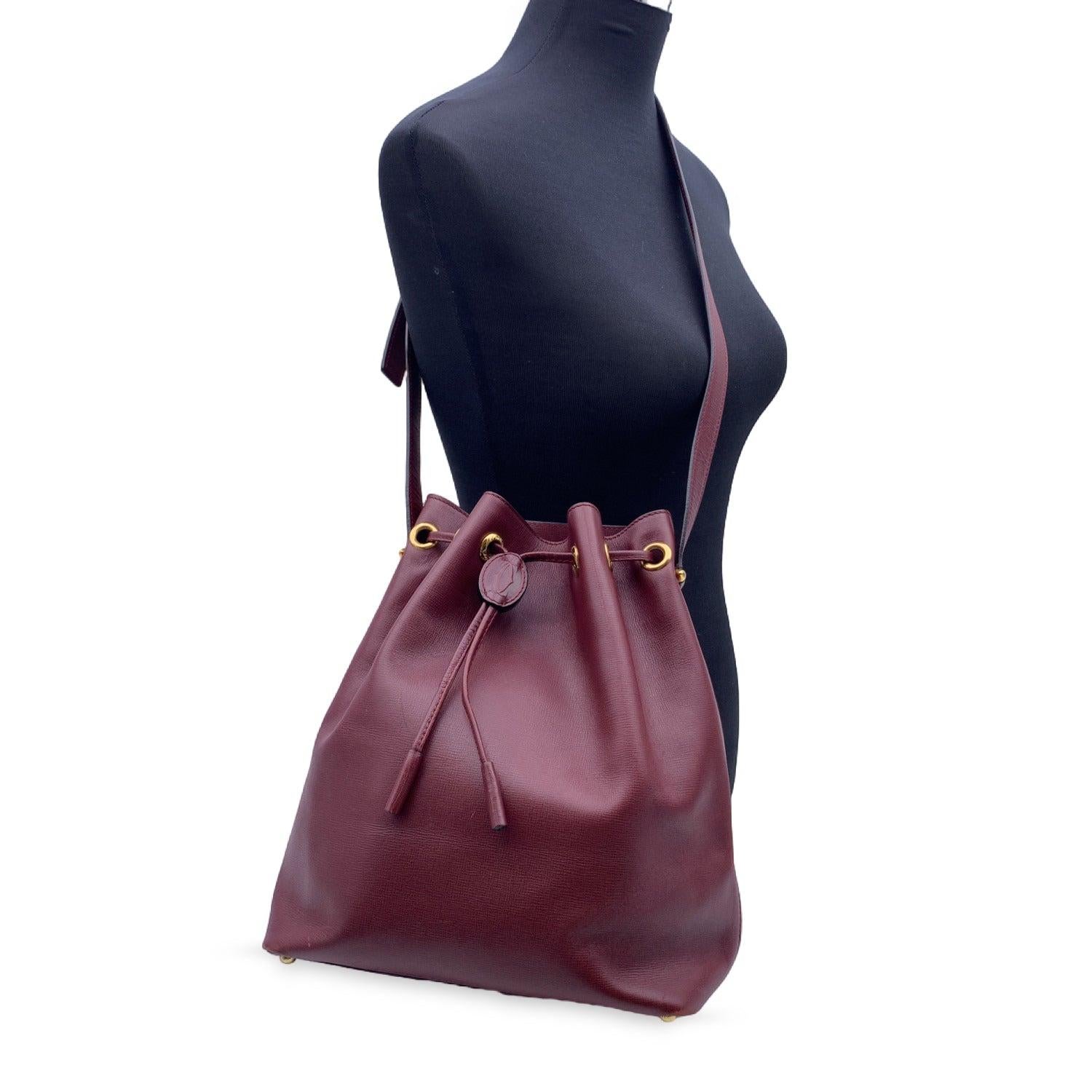 Cartier Vintage drawstring bucket in burgundy genuine leather. Cartier logo patch on the front. Gold metal hardware. Burgundy lining with Cartier logos. 1 side open pocket. Adjustable shoulder strap. 'Cartier Paris' embossed inside Condition A -