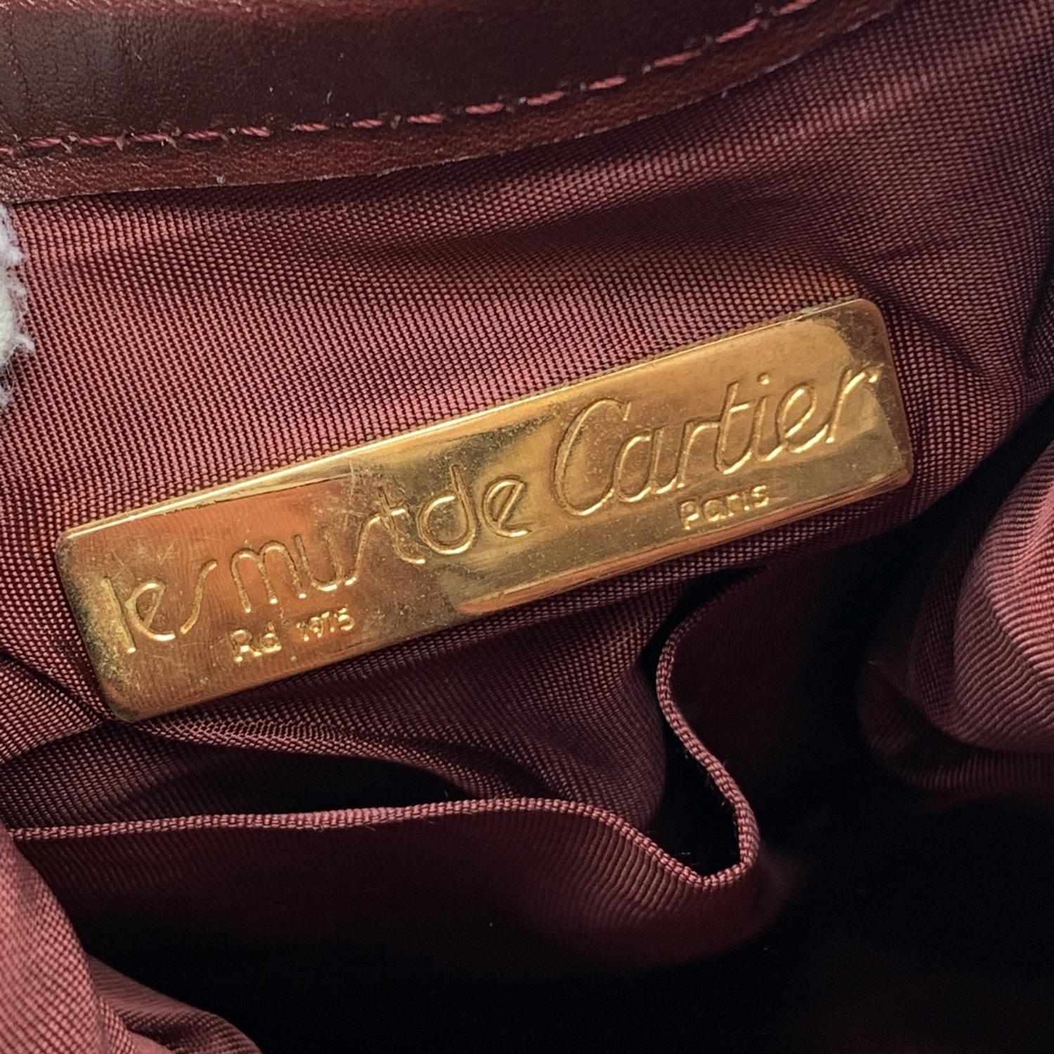 CARTIER Paris Vintage drawstring bucket in Burgundy genuine leather. Cartier logo patch on the front. Gold metal. hardware. Burgundy lining with Cartier logos. 1 side open pocket. Adjustable shoulder strap. 'Must de Cartier' tag