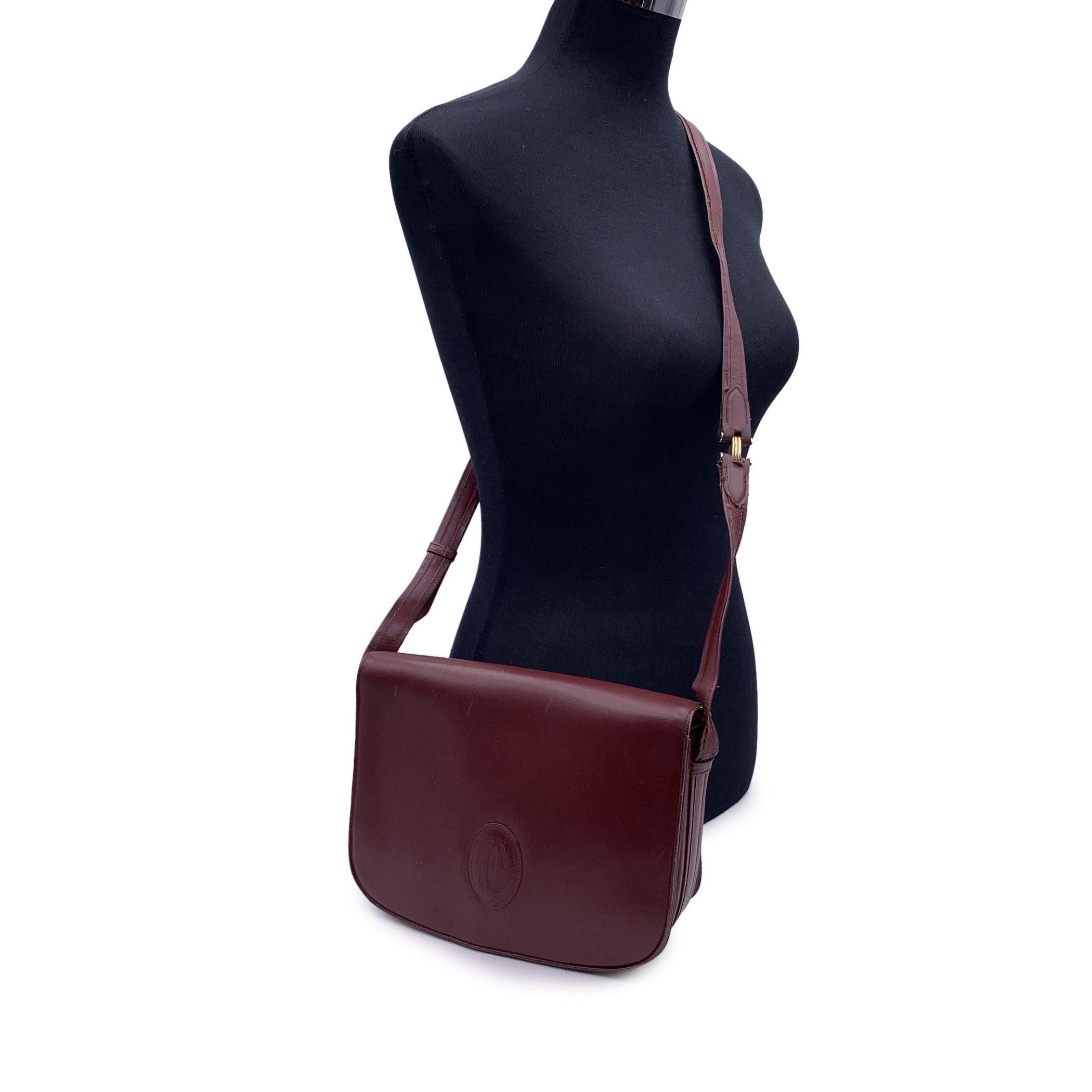 CARTIER Paris Vintage shoulder bag in Burgundy genuine leather. Flap with magnetic button closure. Cartier logo patch on the front. Burgundy lining with Cartier logos. 3 main sections. 1 side zip pocket and 1 side open pocket inside. Adjustable
