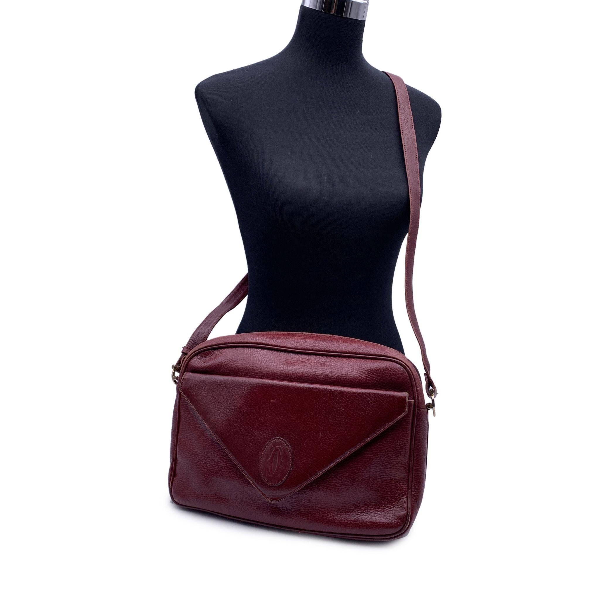 CARTIER Paris Vintage shoulder bag in burgundy genuine leather. Upper zipper closure. 1 front pocket with magnetic button closure. Cartier logo patch on the front. Burgundy fabric lining . 1 side zip pocket inside. Adjustable shoulder strap. 'Must