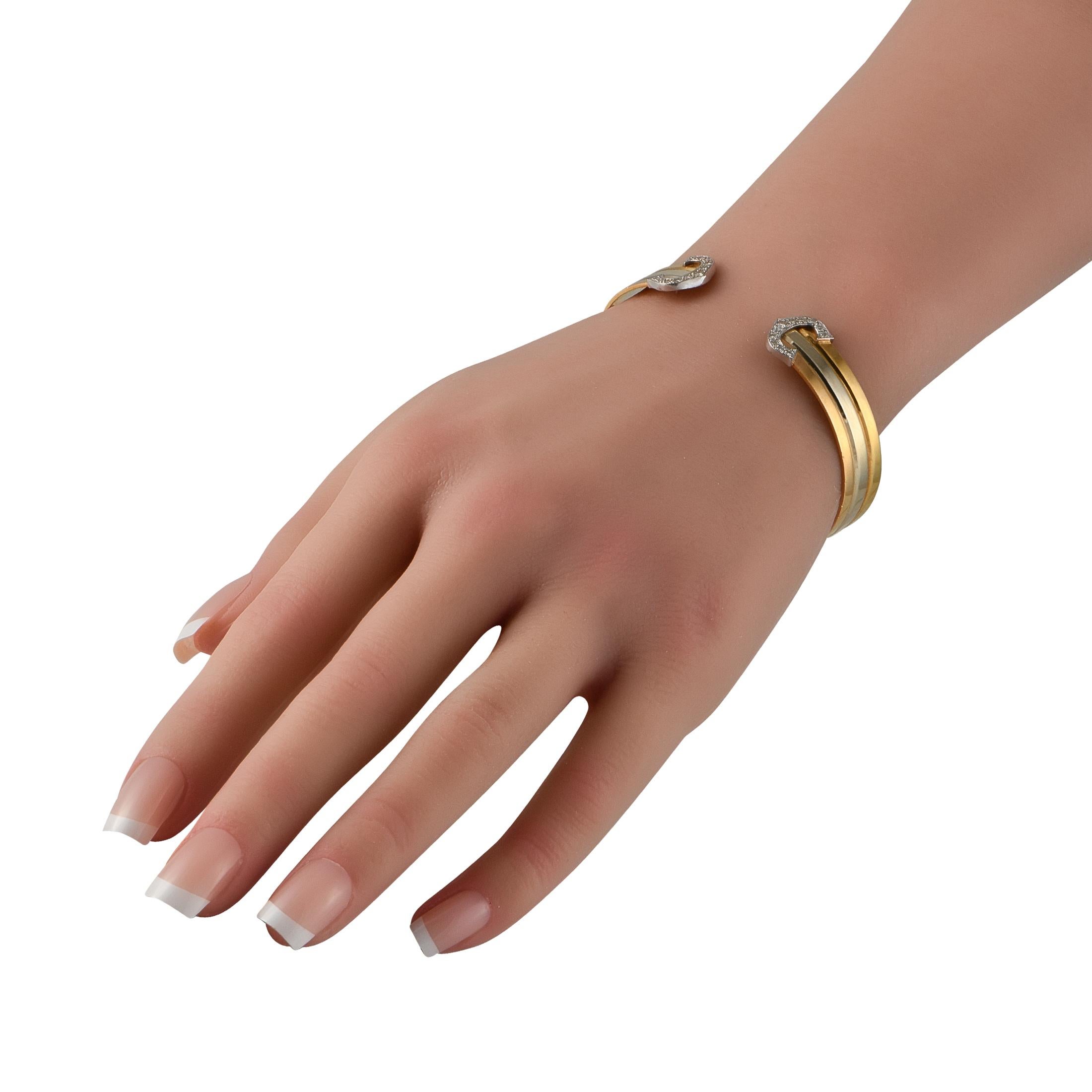 Part of the C de Cartier collection is this tri-gold bangle with a polished cuff band divided into three smaller bandsone in yellow gold, the middle in white gold, and the third in rose gold. The two ends of the band do not meet, each capped by a