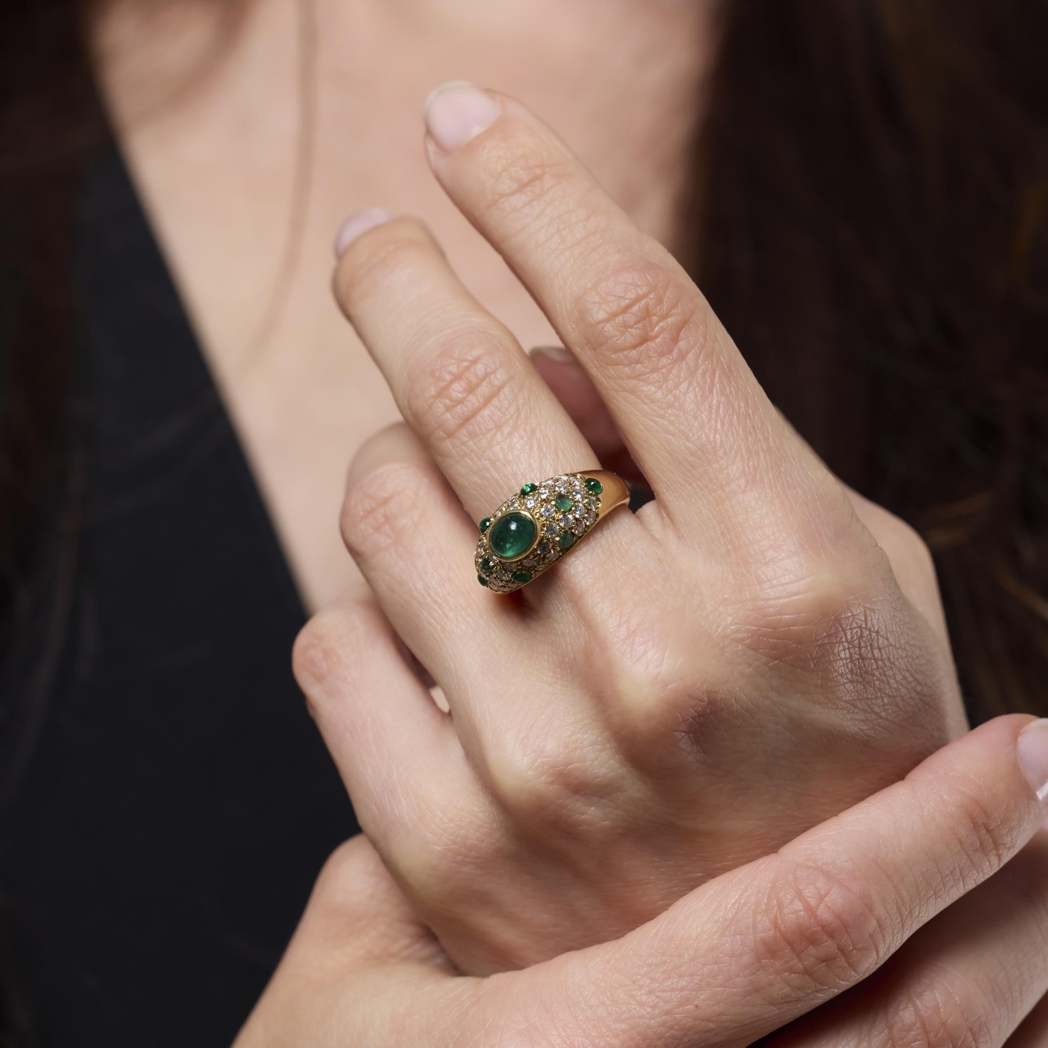 Questo squisito anello vintage di Cartier presenta uno smeraldo cabochon da 0,85 carati circondato da altri smeraldi e scintillanti diamanti taglio brillante. Realizzato in ricco oro giallo 18 carati, incarna il lusso francese senza tempo e