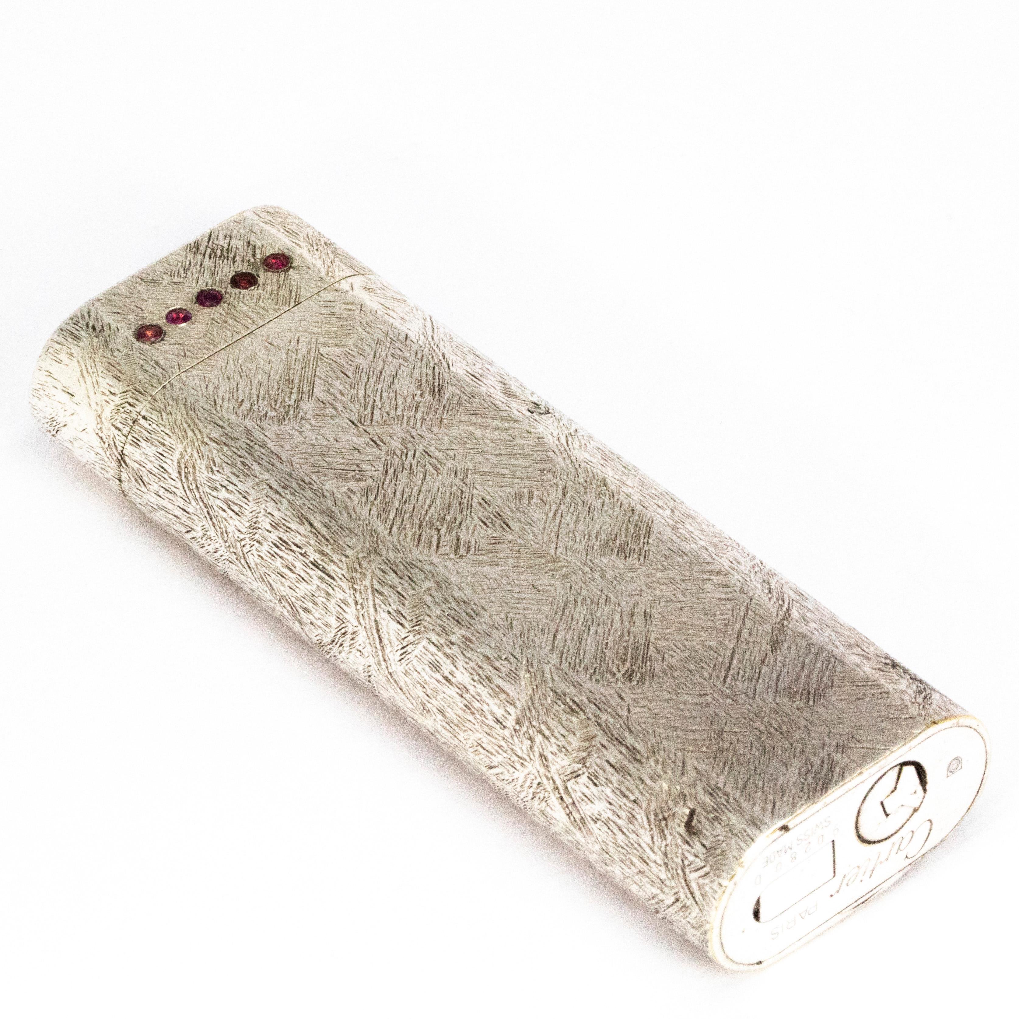 This fancy lighter is modelled in silver and has stylish detail engraved all around it. In the lid there are five rubies set in a line. The red rubies complement the engraved silver beautifully. The Cartier signature can be found on the under side