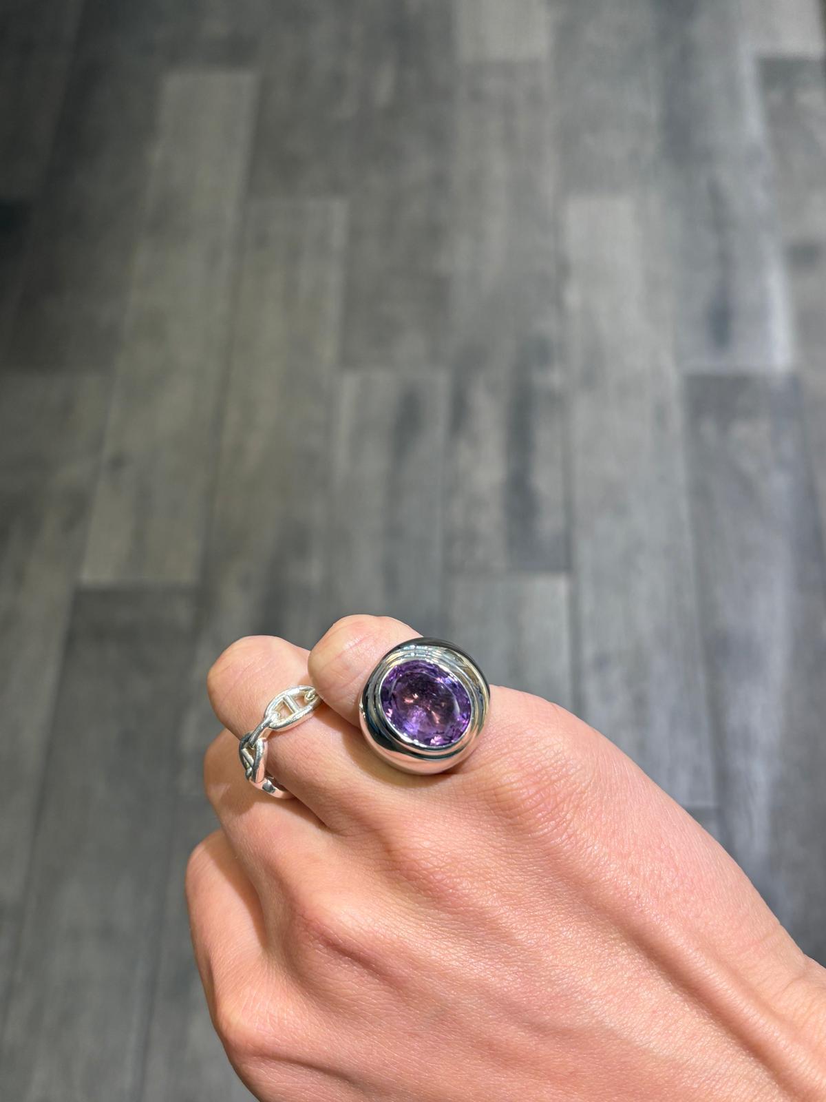 A rather special and delicious Cartier cocktail ring centering a large oval faceted amethyst which is 13mm by 15mm in dimension. The amethyst is attractively bezel set, and the band of the ring is tapered towards the bottom, and is done in a high
