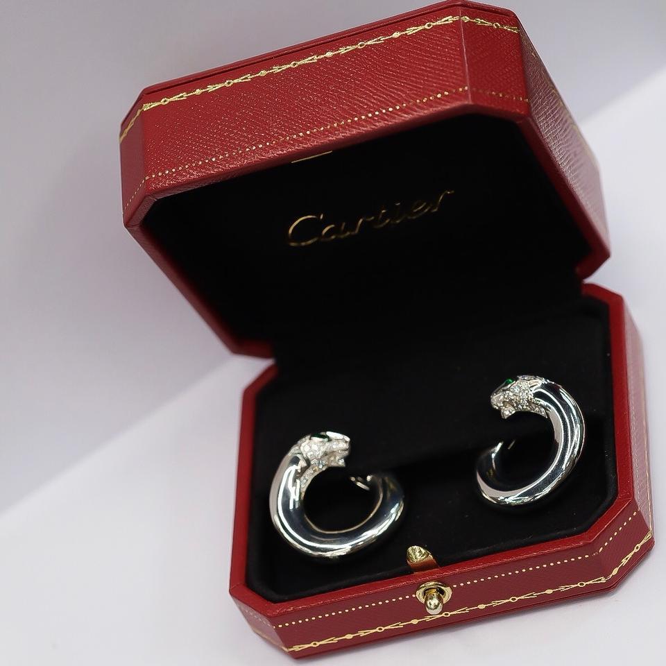 The iconic Cartier Panther in the form of hoop earrings. Formed from 18 carat white gold in perfect hoops with pave diamond set panther heads, each with a single pear shaped emerald eye. With original red Cartier box. Beautiful earrings from one of