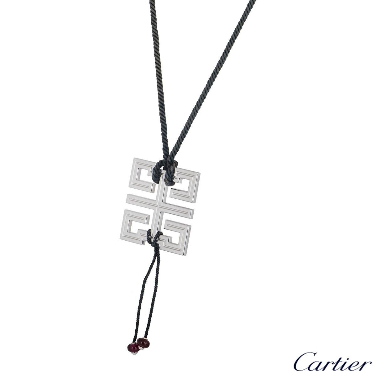 A stylish 18k white gold pendant by Cartier from the Le Baiser Du Dragon collection. The pendant features the dragon motif symbol with a twisted black cord tied and hanging at the bottom are two ruby beads. The pendant comes with an adjustable cord