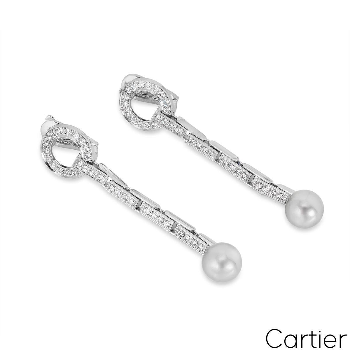An impeccable pair of 18k white gold pearl and diamond earrings by Cartier from the Agrafe collection. The earrings comprise of a diamond set open work circular motif and 4 diamond set freely moving stations that lead to a 10mm light grey pearl. The
