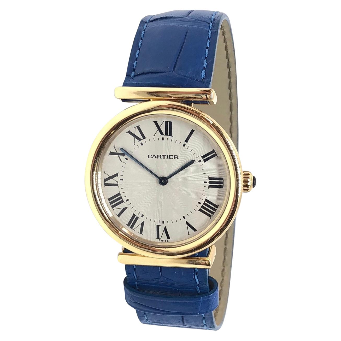Classic round Cartier Bi-Plan timepiece with a unique hidden clasp. Brand new french blue Cartier leather strap. Excellent like-new condition, no scratches or wear. 

•MOVEMENT: MECHANICAL HAND WINDING
•CASE MATERIAL: 18K YELLOW GOLD
•CONDITION: