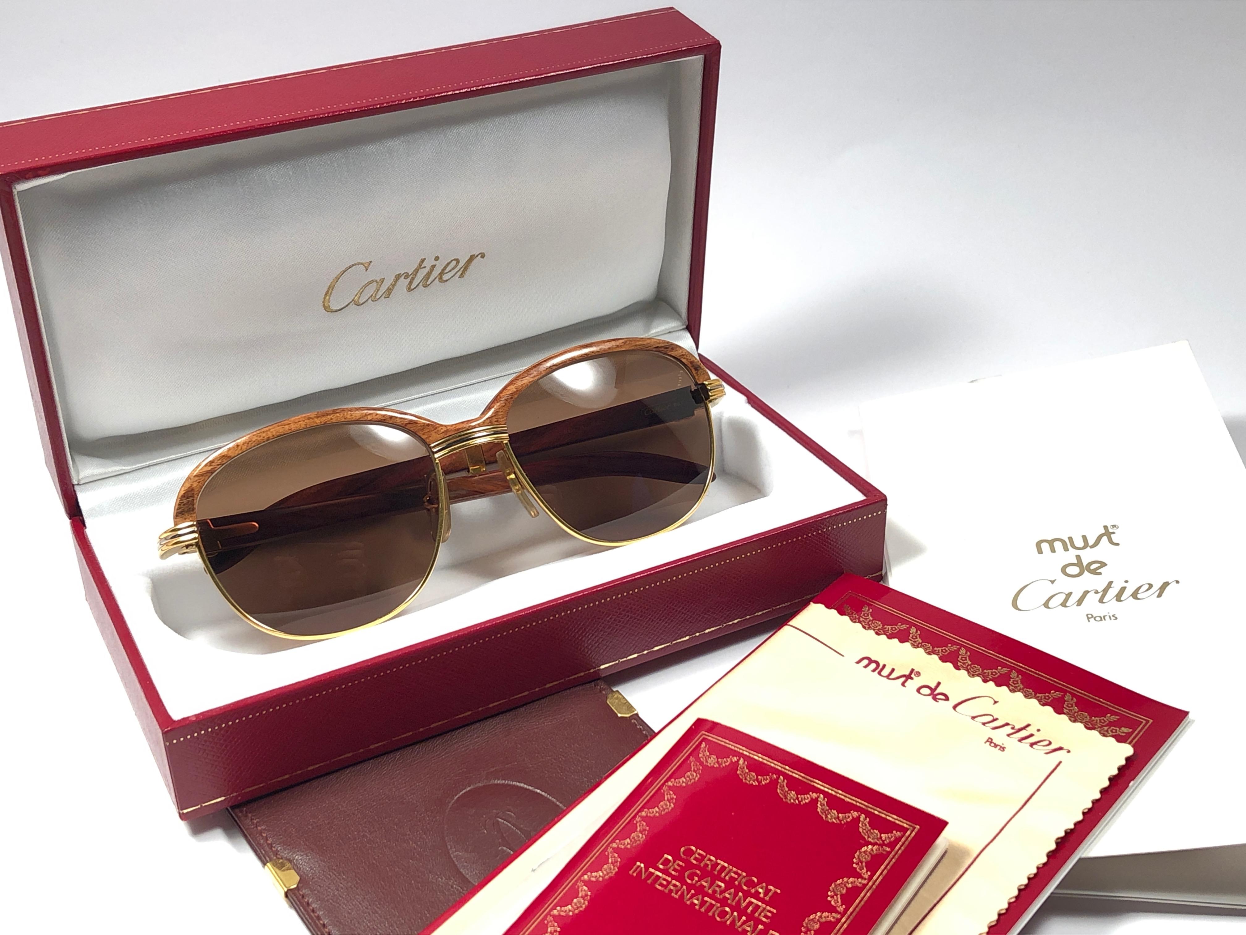 Lunettes de soleil d'origine 1990 Cartier Malmaison en bois dur avec verres marron miel (protection contre les UV). 
Façade et flancs en or jaune et blanc et possède la fameuse façade en bois. Les temples sont également en palissandre combiné avec