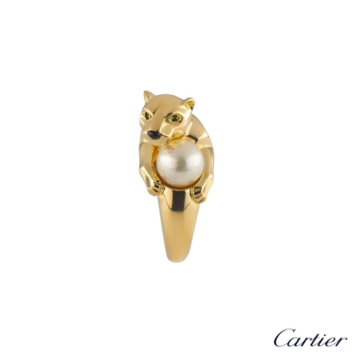 A unique 18k yellow gold Panthere ring by Cartier. The ring features a Panthere's head with two emeralds set to the eyes and onyx for the nose. The panthere is clutching an 8mm cultured pearl between the paws. The Panthere measures 1.4cm in height