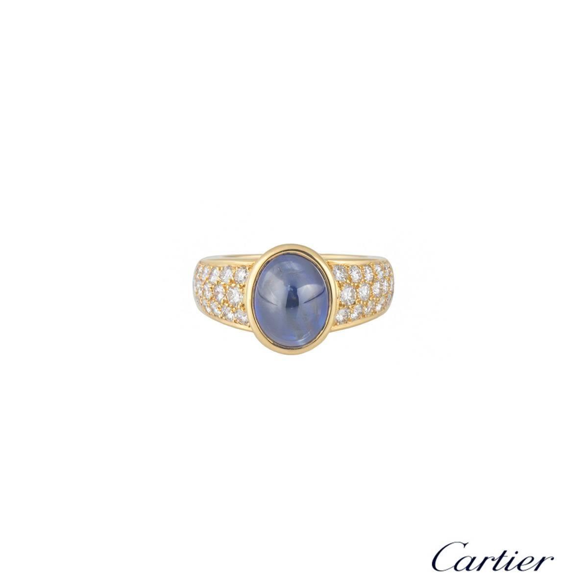 A beautiful 18k yellow gold diamond and sapphire Cartier dress ring. The ring comprises of an oval cabochon cut sapphire in a rubover setting set to the centre with a weight of approximately 3.85ct, with a dark blue hue throughout. Complementing the
