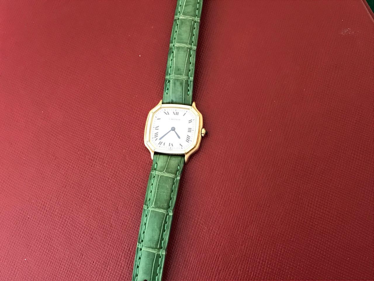 Cartier Pre Owned Ladies Manual Winding wrist watch. White Dial with black Roman numerals. 18k Yellow Gold octagonal style case with Blue Sapphire cabachon setting crown (25x28mm). Dark green strap with 18k Yellow Gold Cartier buckle. Inventory