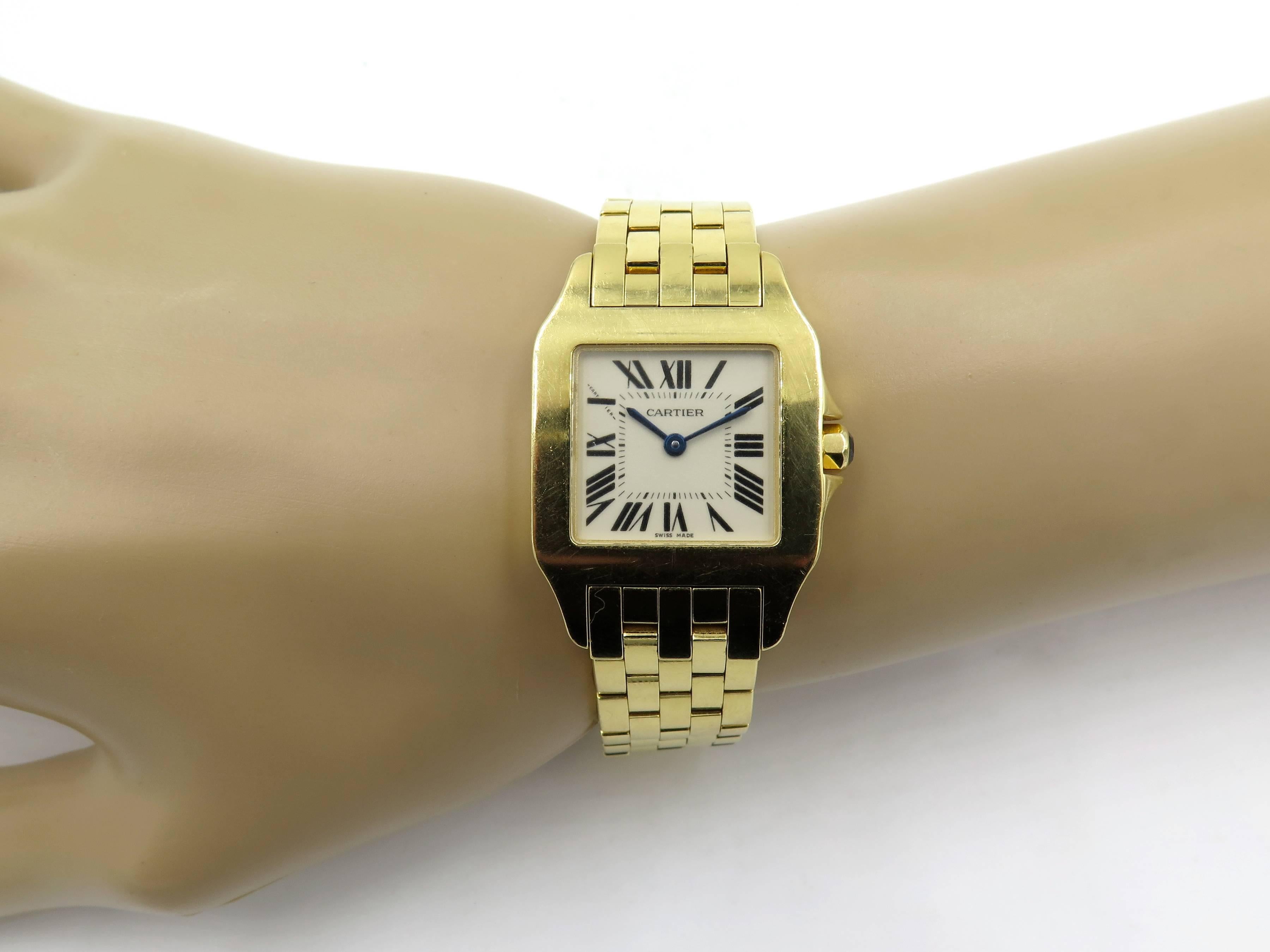 An 18 karat yellow gold Santos Demoiselle watch. Cartier. Model number 2702.  Midsize. 26mm. Of quartz movement, the cream dial with black Roman numerals and blued steel hands, secret signature at 10 o’clock, joined by a polished gold brick link