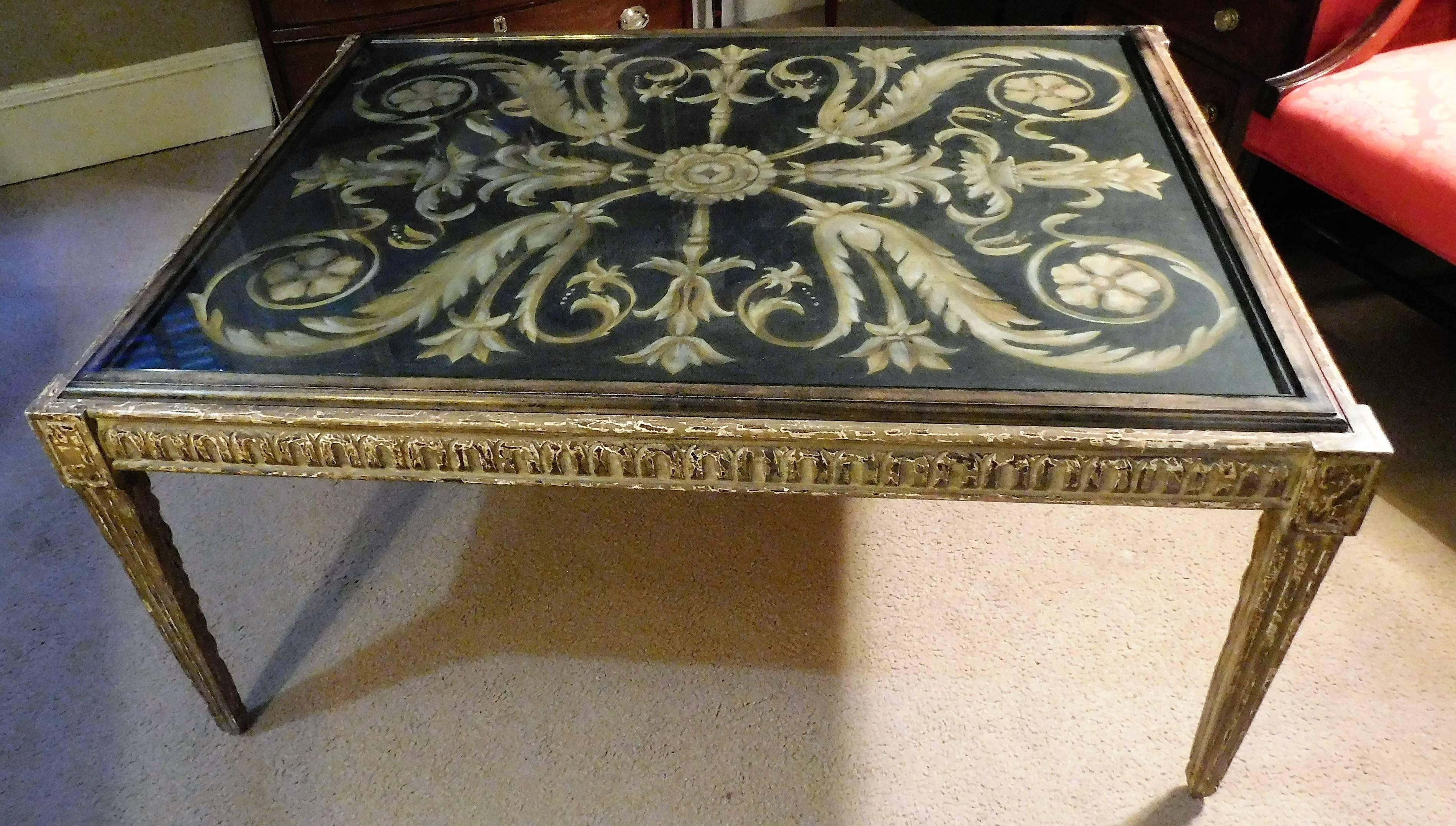 A large bench-made carved and painted wooden coffee table with canvas painted top. Bold Baroque design in muted colors under glass. Faux aged legs and skirt. Signed 