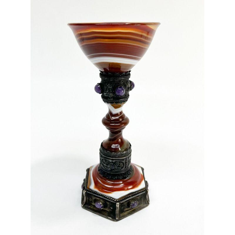 Carved Agate & silver mounted goblet with amethyst cabochon jewels, 19th century

Continental carved banded agate wine vessel with gem set silver mounts. Silver mount under the bowl adorned with grape leaf motifs and the faces of Bacchus the Greek