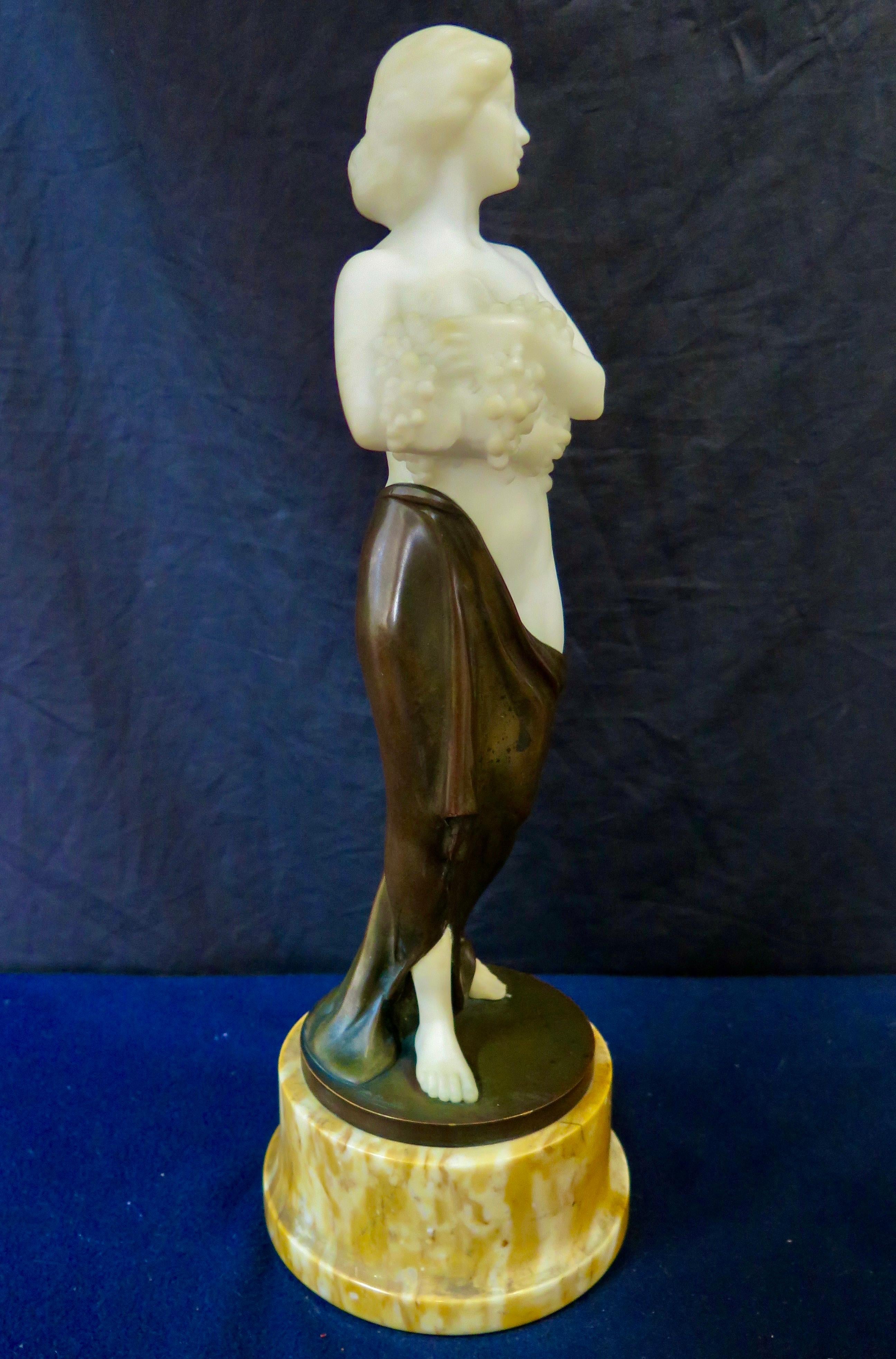 This vintage patinated bronze & hand carved alabaster figural sculpture dates from the early 20th century. The sculpture depicts a shapely semi nude young woman in a draped skirt descending from her hip. She modestly conceals her breasts by holding