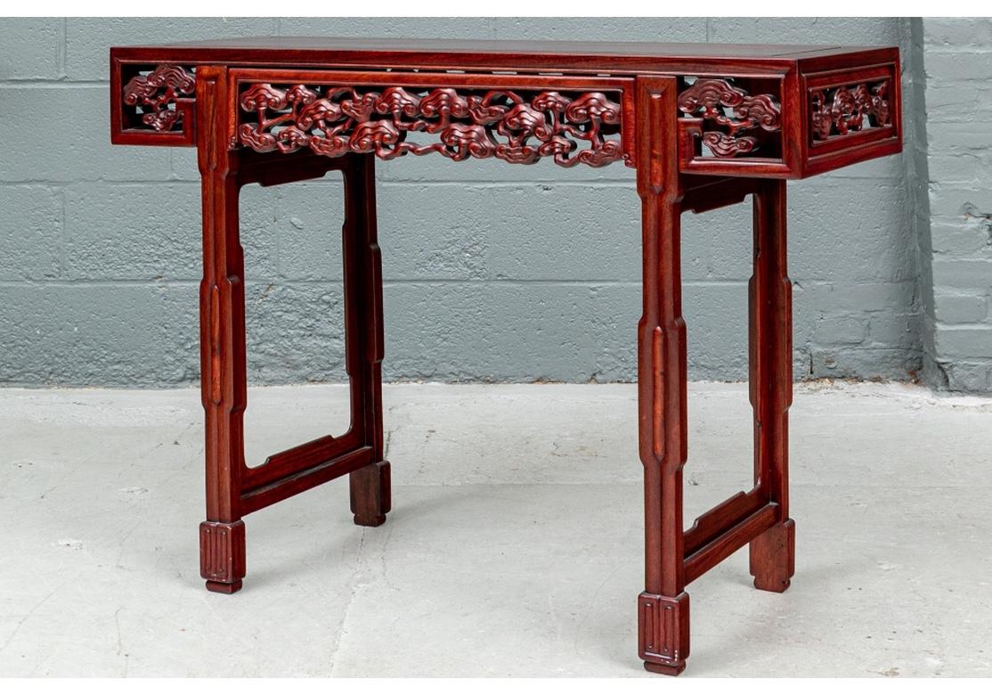 Diminutive Asian console table with elaborate carved openwork apron in panels with rippling and curved cloud motifs on all sides. The top with carved inner panel mounted on tall carved legs. The angular legs with raised details and inner shaped side