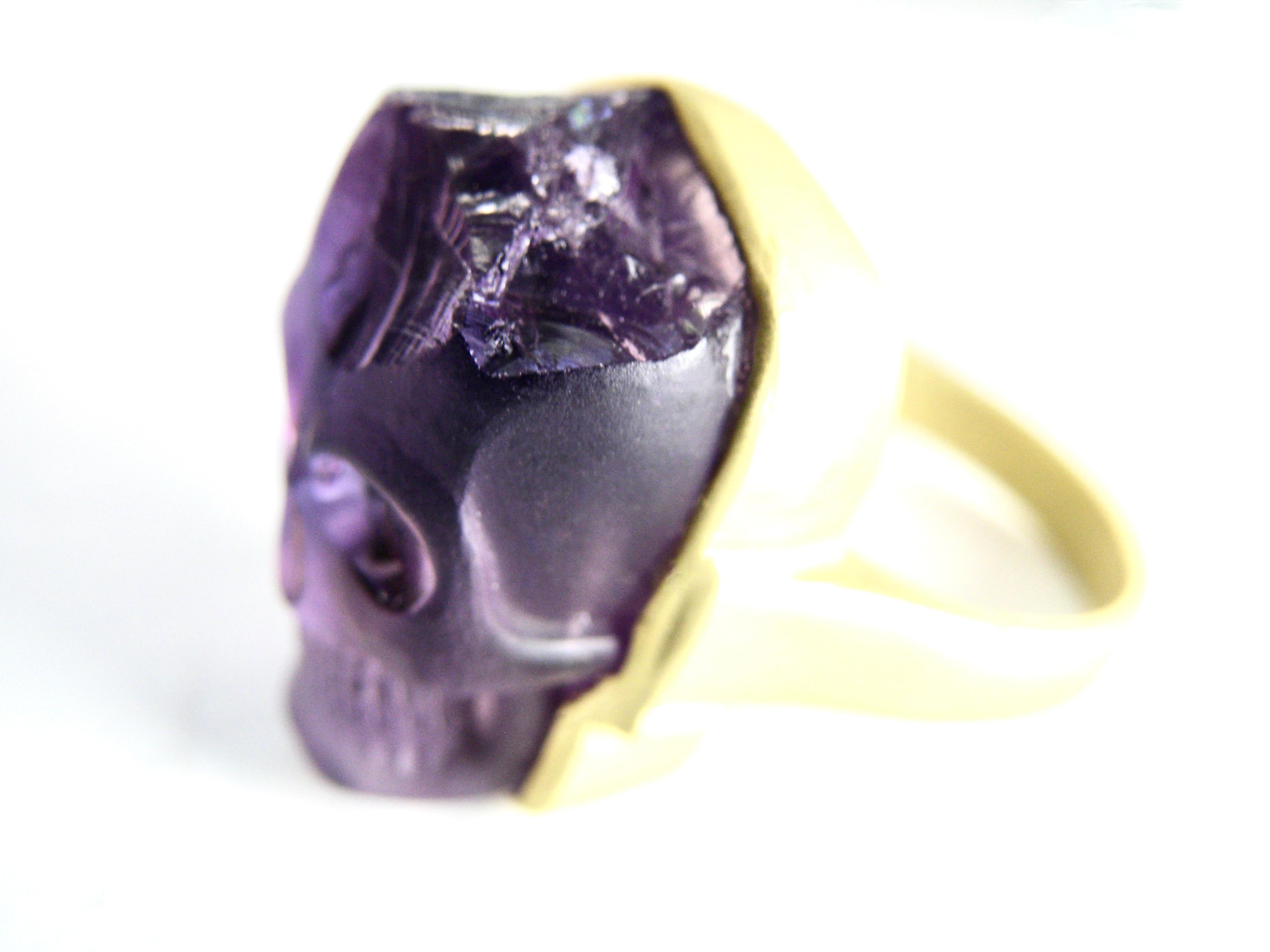 Hand carved skull in Amethyst crystal. 18k matte gold ring. A part of the raw crystal amethyst is exposed just above the forehead.