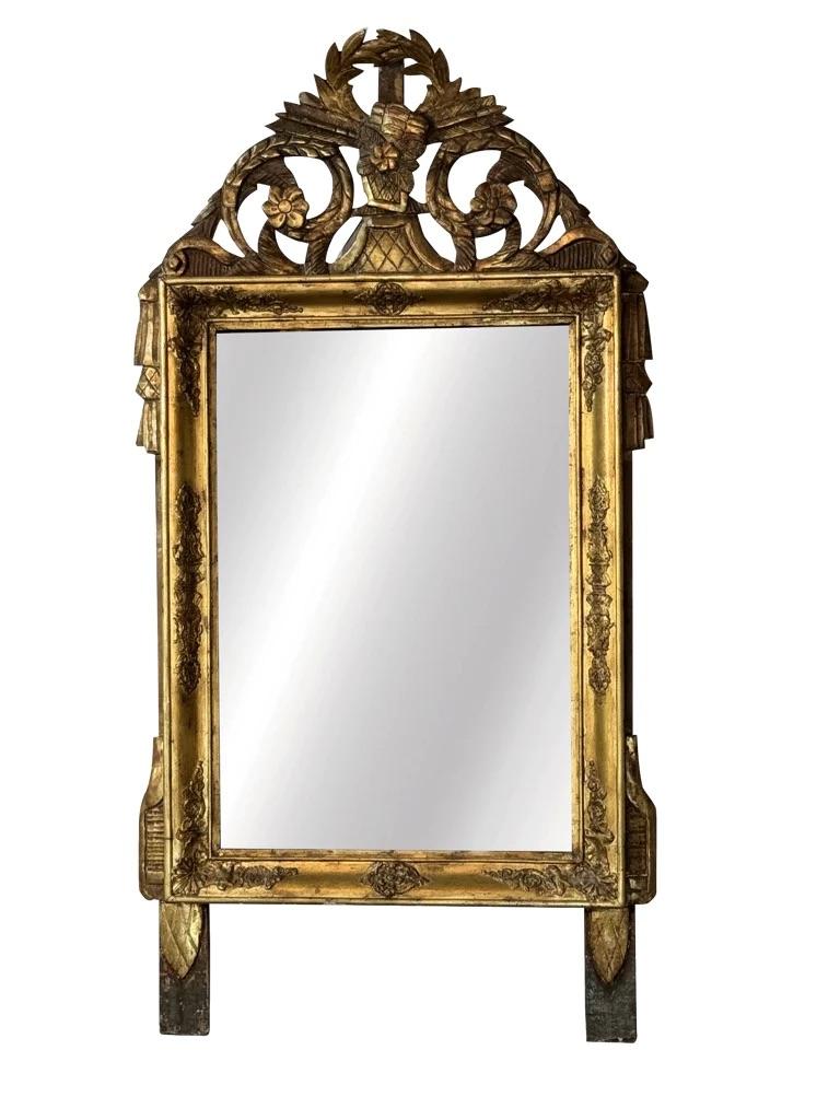 Lovely late 18th-early 19th Century French Provincial Mirror,  well carved and gilded, having astrong crest with laurel leafs, quivers,floral, and drape motifs over a rectangular frame having further carved detail. The mirror plate is early and