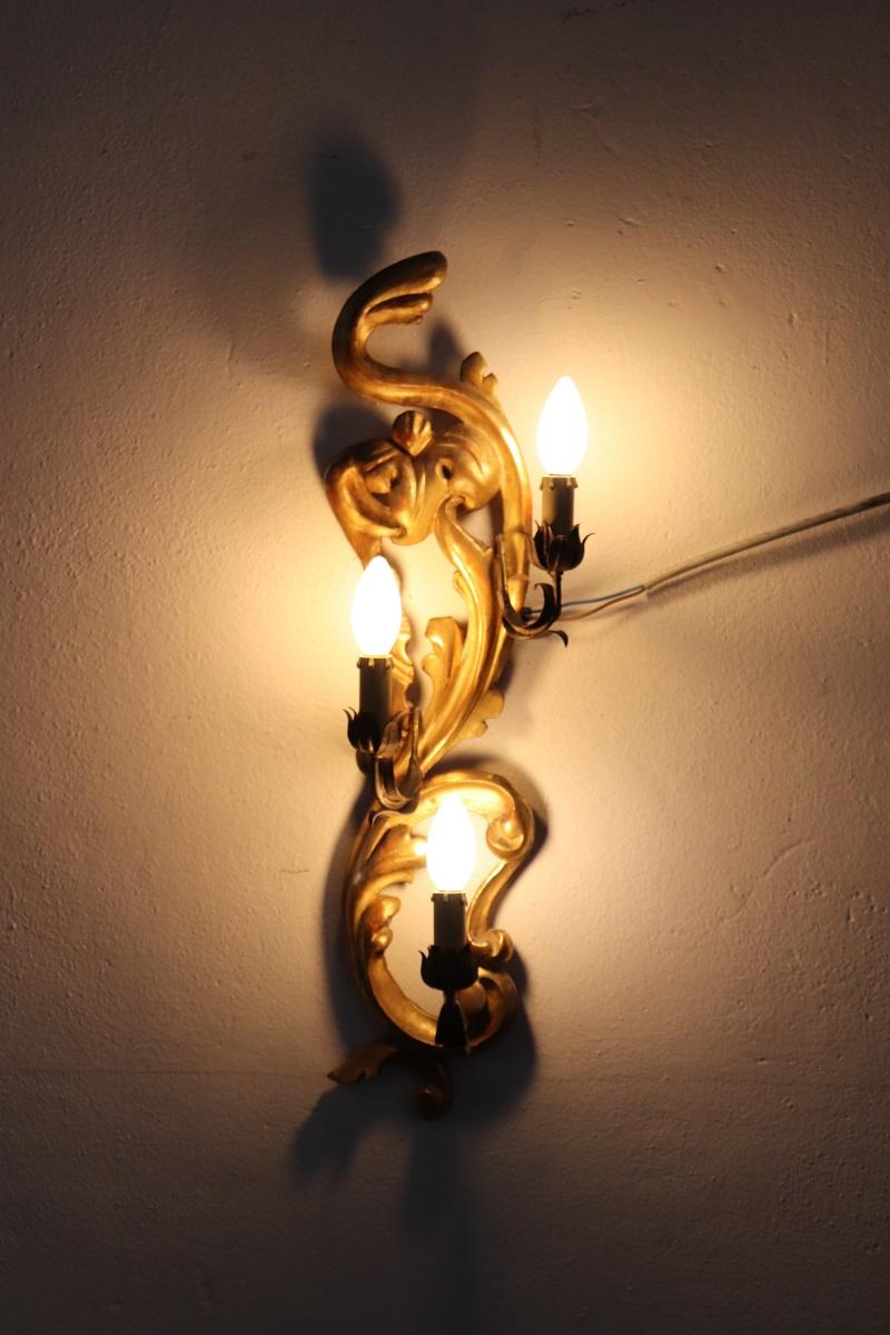 Este exquisito aplique es un verdadero testimonio de la suntuosa artesanía de principios del siglo XX. Fabricada con madera magistralmente tallada y adornada con un delicado dorado en pan de oro, desprende una elegancia atemporal que recuerda a la