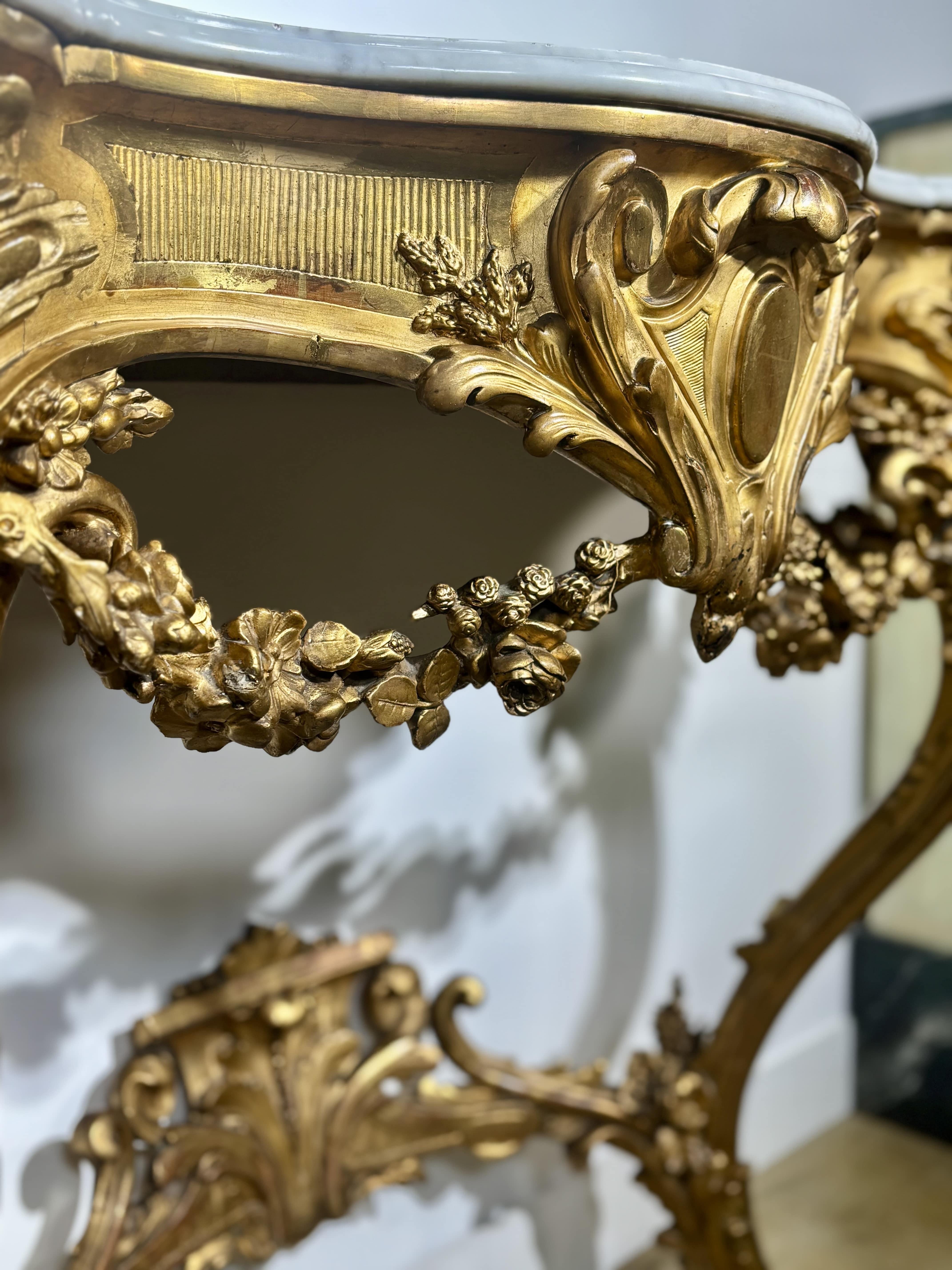 Table console en bois finement sculpté et doré, à décor Rocaille de rinceaux, feuilles d'acanthe, cartouche central, coquilles et guirlandes florales.  
La base incurvée est reliée à une entretoise ajourée à décor de feuillages.  Plateau gaufré en