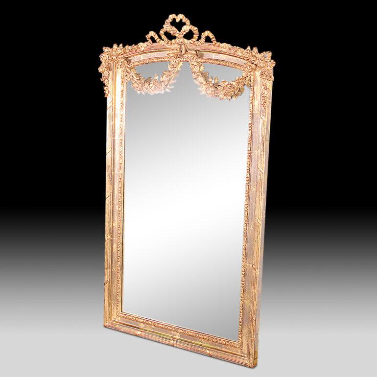 Highly-detailed gilt carved Louis XVI style mirror, the arched top with finely-carved ribbons and swags, the sides and bottom of the frame with reeded classical details. Antiqued 'hazing' or sutle sparkle to the glass itself.



