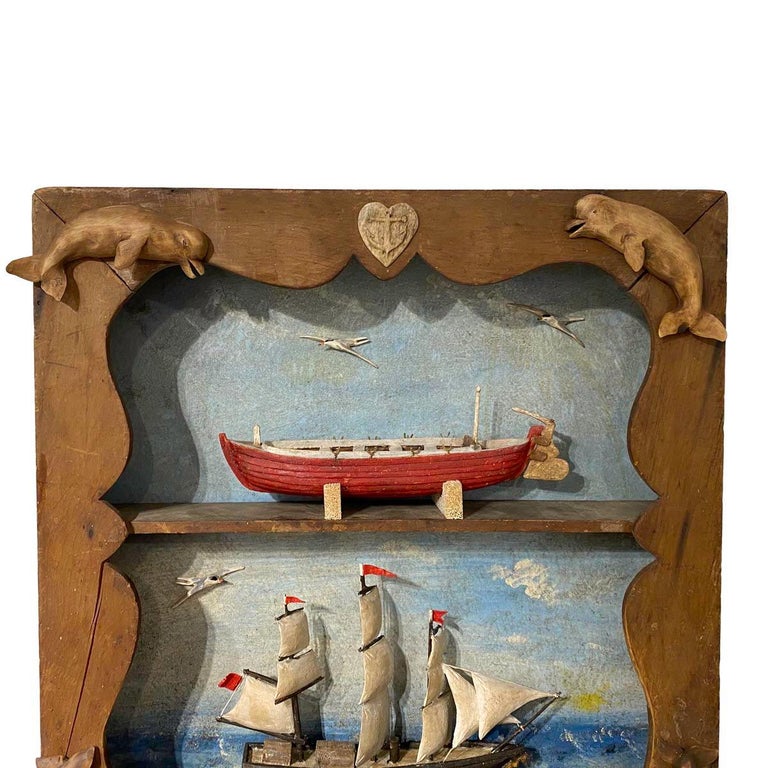 A carved and painted double diorama by master carver Frank Finney. The top half with a red whaleboat, the lower half with a whaleship under sail. The background painted with water and sky and with applied carved birds in flight. I a shaped frame