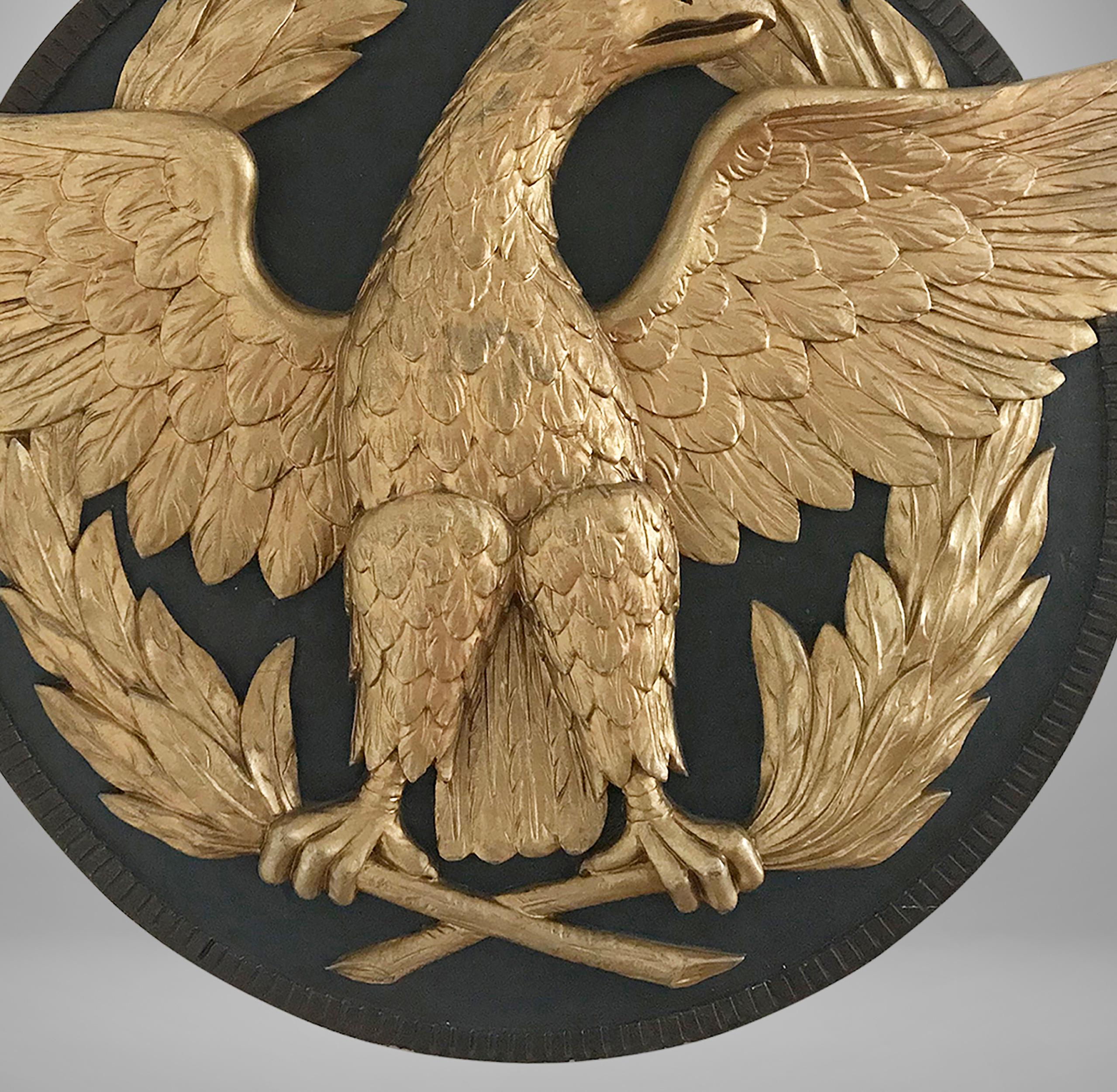 Unusual form and highly detailed that was masterfully carved in relief form in three sections, most likely used on a Government building. The eagle is clutching two long olive branches that go around the roundel up to the head. The roundel is