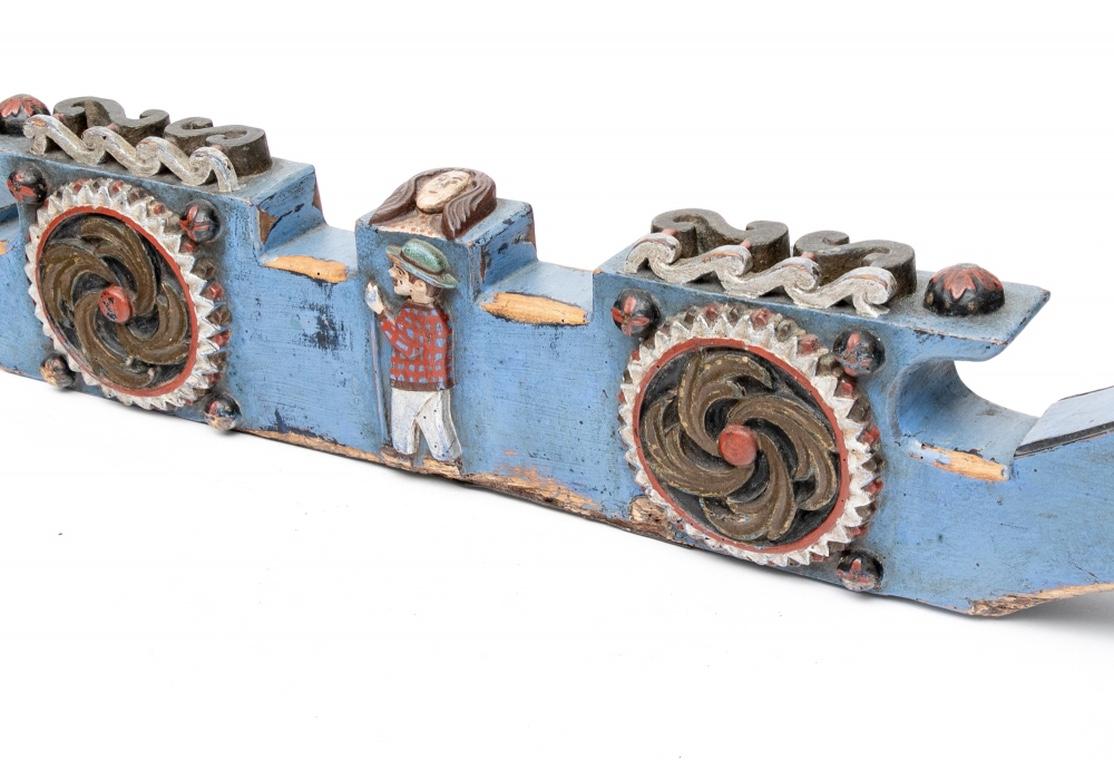 A long shaped piece with scrolled ends in blue paint, decorated with relief carved rosettes and a male figure walking on the front. The top with scrolls and female face in the center. The back with scrolled Primitive style floral decorative motifs