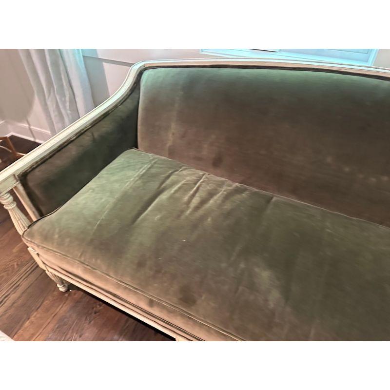 A carved and painted Louis XVI style sofa with green velvet upholstery. This expertly crafted Louis XVI style sofa is a true masterpiece of artistry and sophistication. The intricately carved wooden frame showcases the opulence and refinement