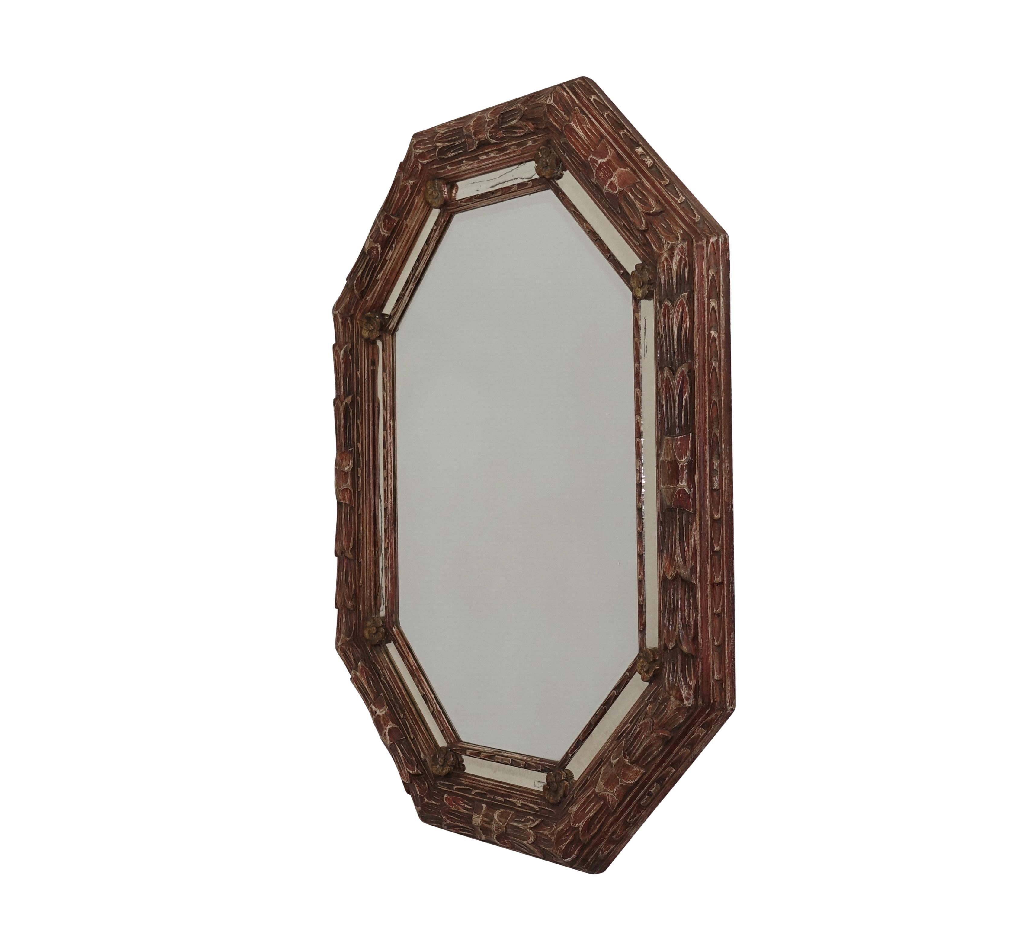 Octagonal shape leaf carved bullnose framed mirror with rosettes, having a red and white painted finish. The vintage mirror shows age and some clouding, Continental, mid-20th century. 
 