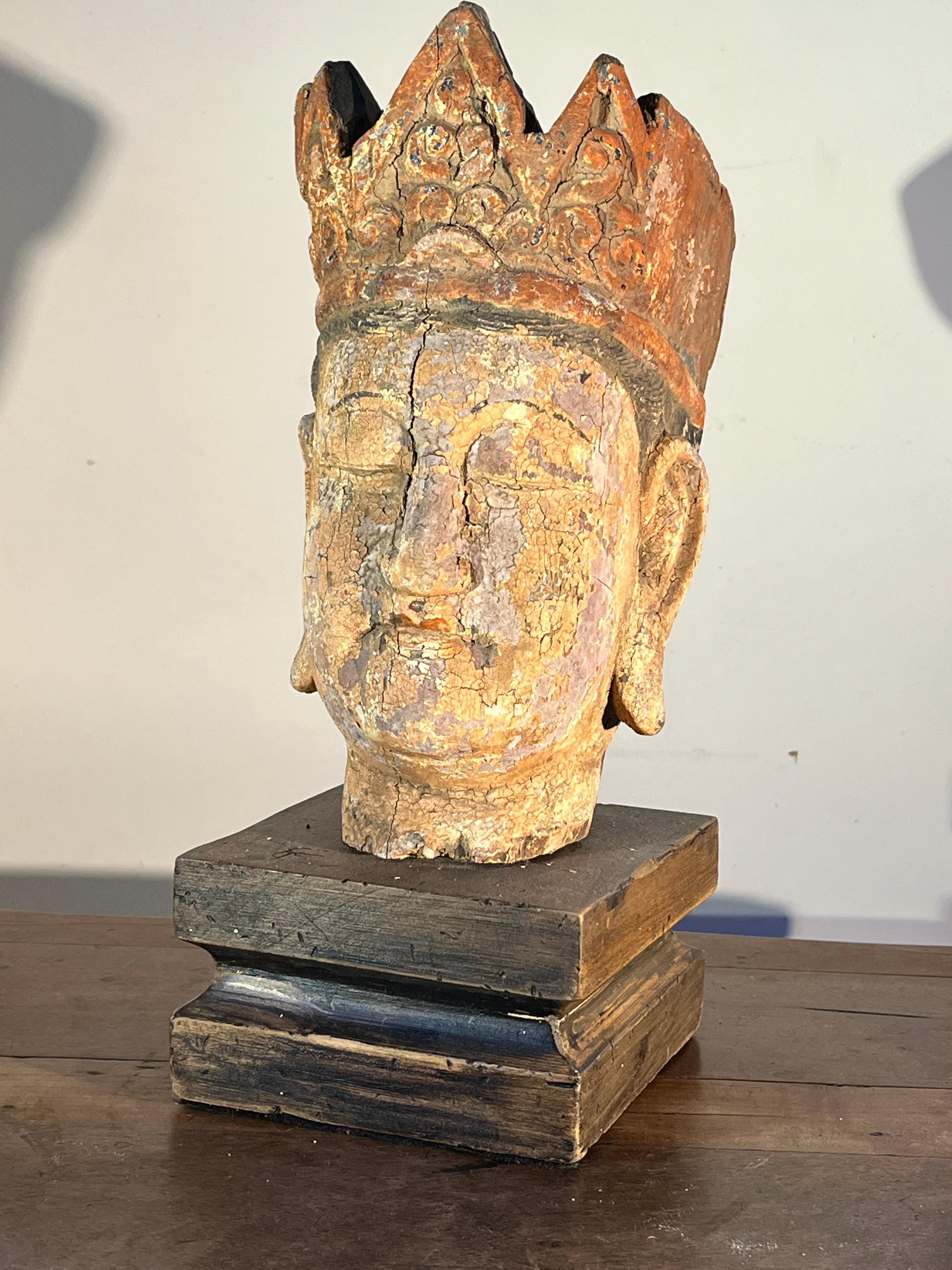 A Chinese carved-wood Buddha head retaining its original polychrome painted finish, 18th century or earlier, now mounted on a wood stand. Head measures 10” high without stand. 