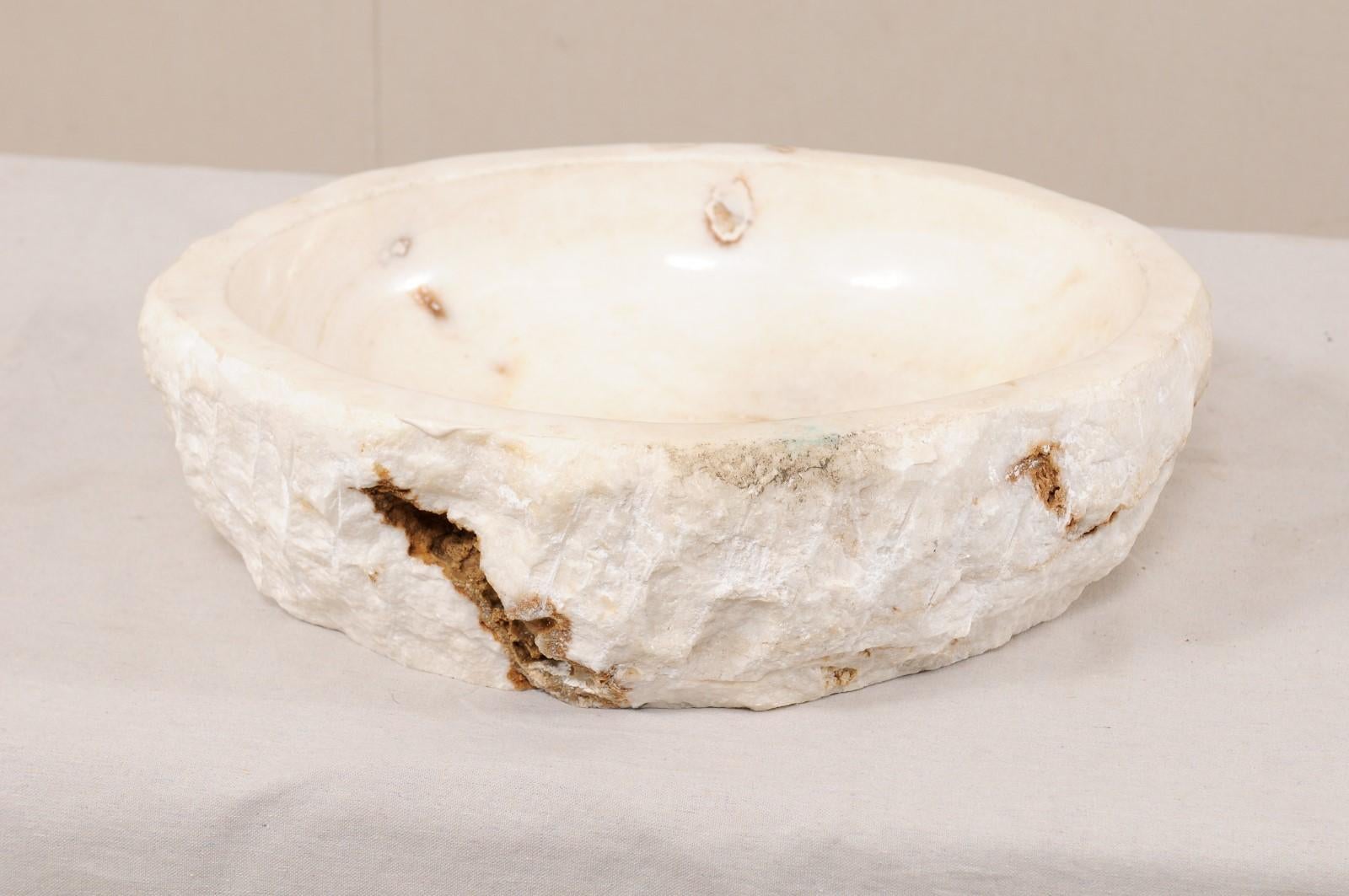 A single natural onyx sink basin with original live edge. This carved vessel sink, created from a rough onyx rock, has a carved and then polished interior basin, making for easy clean-up. The natural textured stone remains about the exterior of the