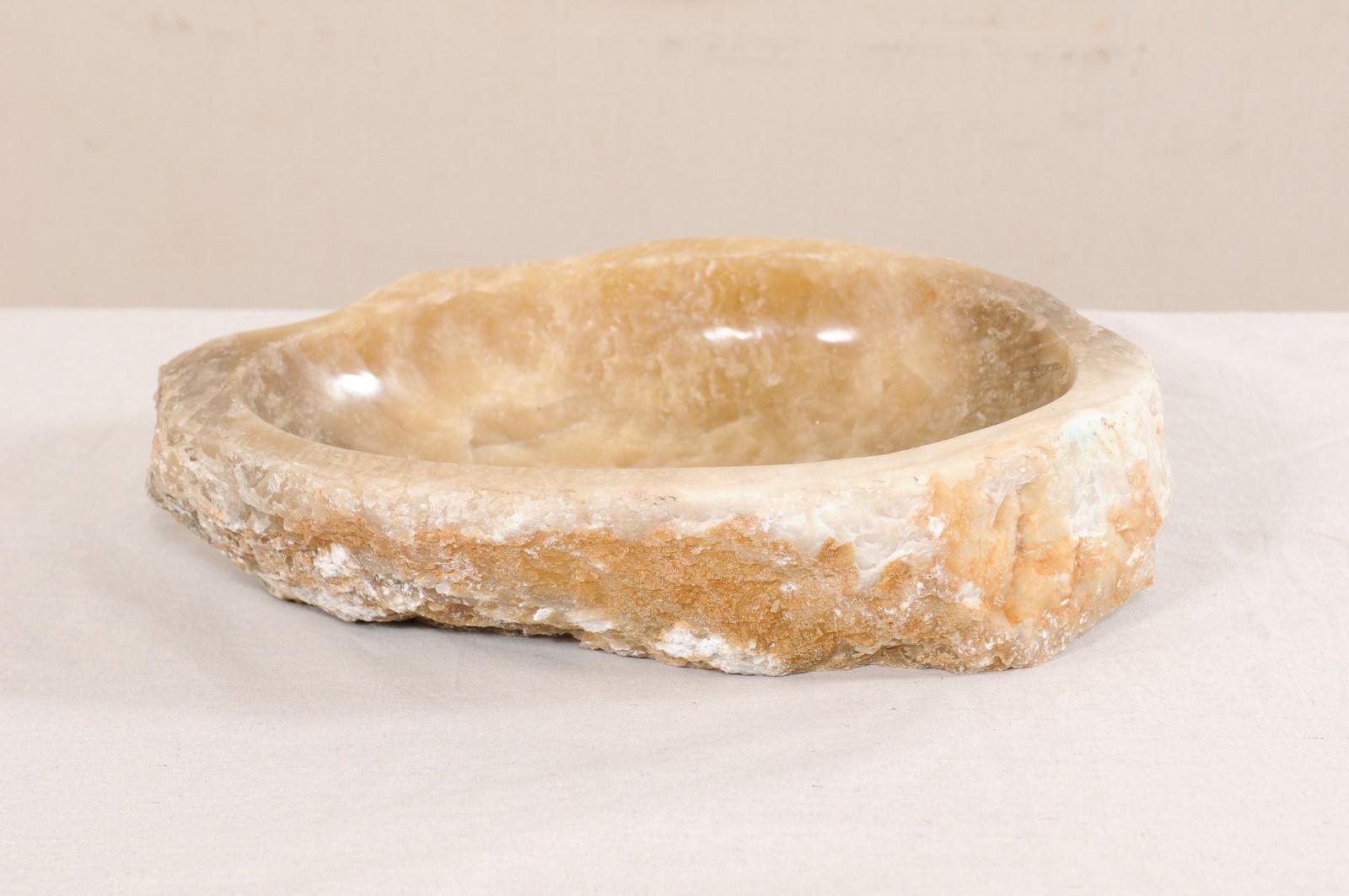 Une vasque en onyx naturel avec bord vif d'origine. Cet évier sculpté, créé à partir d'une roche brute d'onyx, est doté d'un bassin intérieur sculpté puis poli, ce qui facilite le nettoyage. La pierre texturée naturelle reste sur l'extérieur de