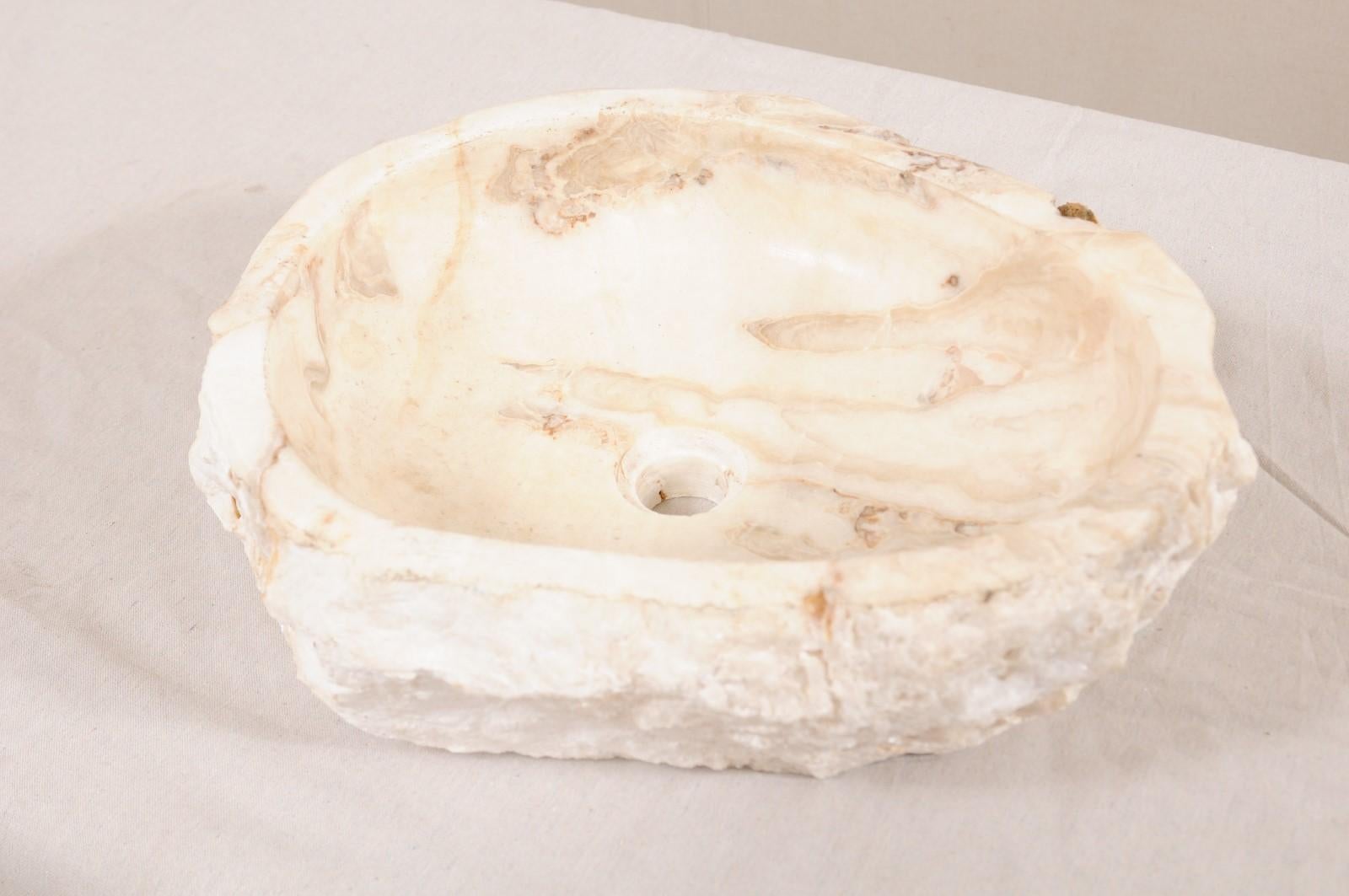 A single natural onyx sink basin with original live edge. This carved vessel sink, created from a rough onyx rock, has a carved and then polished interior basin, making for easy clean-up. The natural textured stone remains about the exterior of the