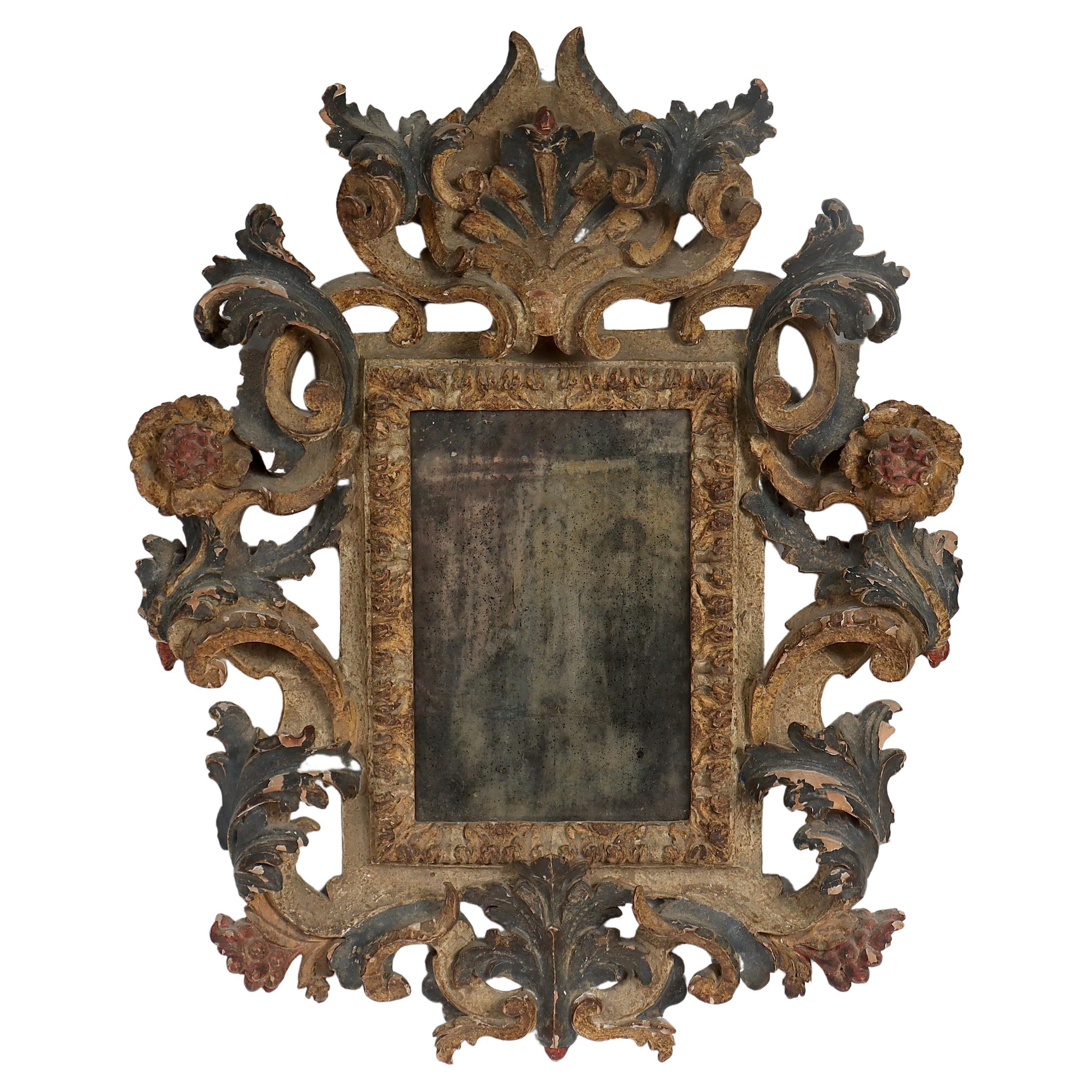 A fine old or antique carved, gessoed, and polychrome painted (Italian Rococo or Florentine style) mirror.

Carved with flowers, rocaille swags, berries and fruit, acanthus leaves, and a shield device to the top. 

Set with a mirrored glass (that